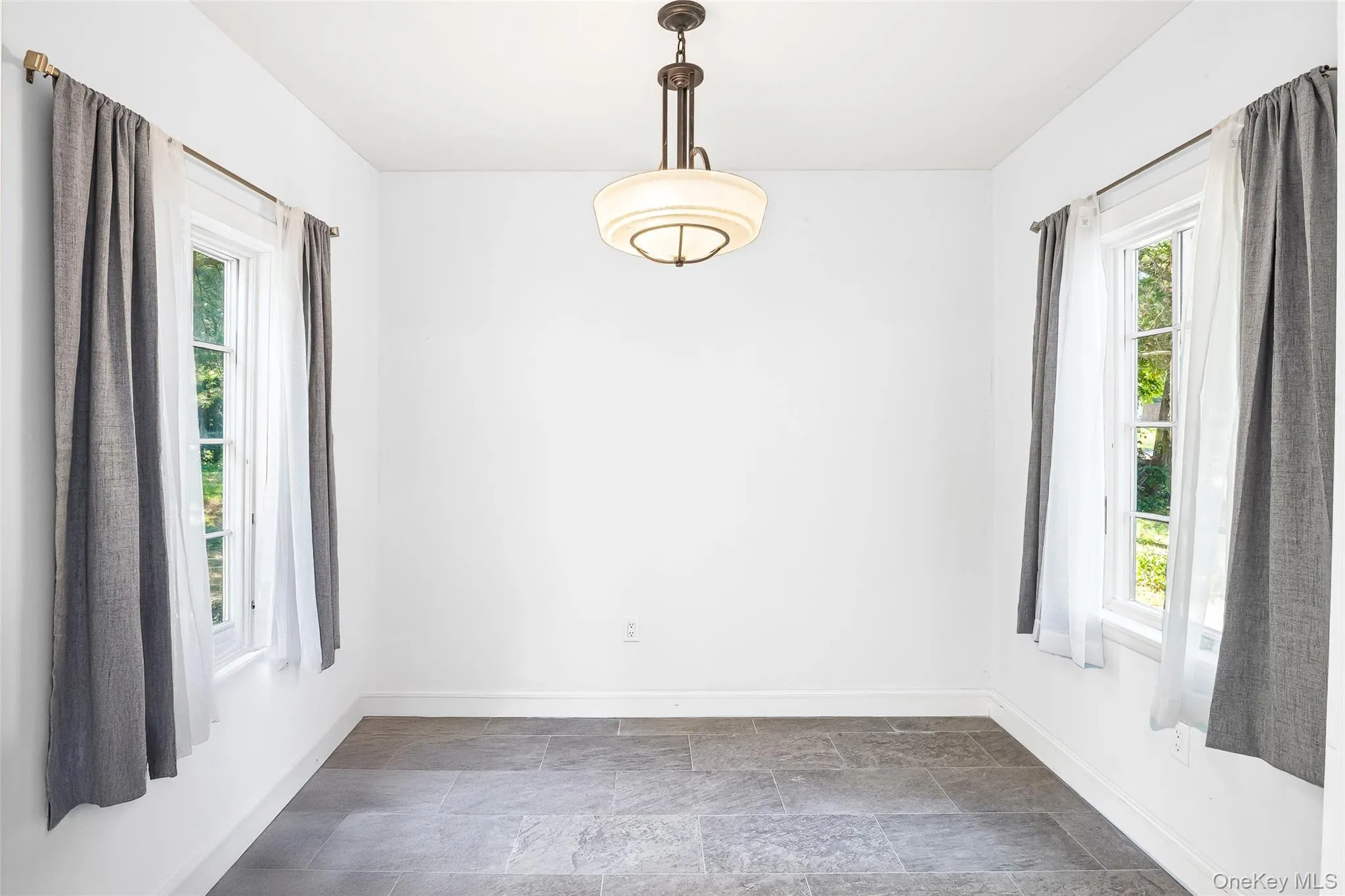 Unfurnished dining area with baseboards and dark stone finish floors Unfurnished dining area with baseboards and dark stone finish floors
