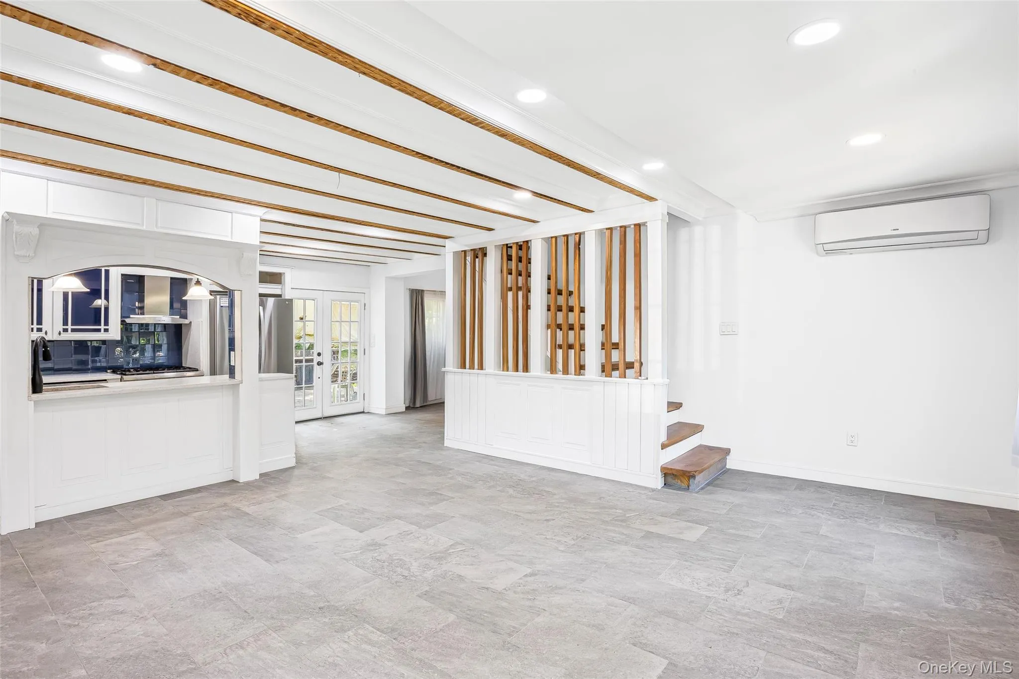 Unfurnished living room featuring french doors, recessed lighting, a wall mounted AC, beamed ceiling, and stone finish flooring Unfurnished living room featuring french doors, recessed lighting, a wall mounted AC, beamed ceiling, and stone finish flooring