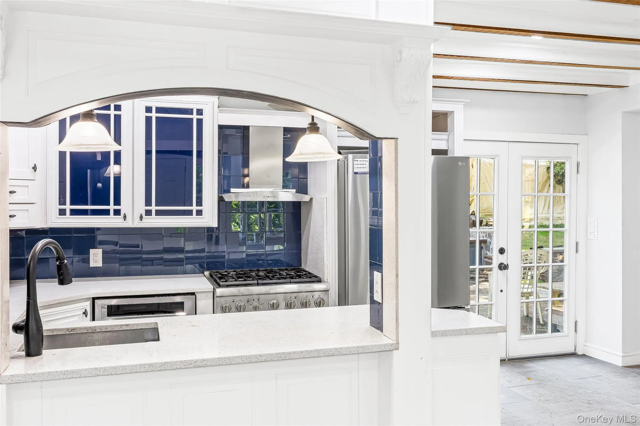 Kitchen with backsplash, white cabinets, french doors, wall chimney exhaust hood, and light stone countertops Kitchen with backsplash, white cabinets, french doors, wall chimney exhaust hood, and light stone countertops