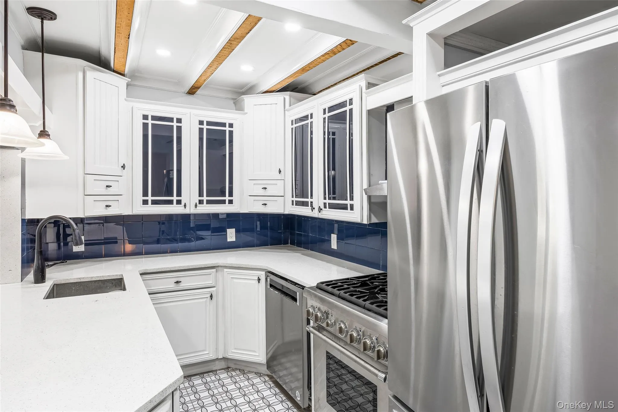 Kitchen with stainless steel appliances, hanging light fixtures, white cabinets, backsplash, and beamed ceiling Kitchen with stainless steel appliances, hanging light fixtures, white cabinets, backsplash, and beamed ceiling