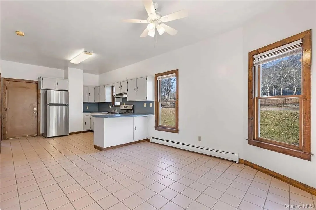 Kitchen featuring freestanding refrigerator, a baseboard heating unit, dark countertops, a peninsula, and light tile patterned floors Kitchen featuring freestanding refrigerator, a baseboard heating unit, dark countertops, a peninsula, and light tile patterned floors
