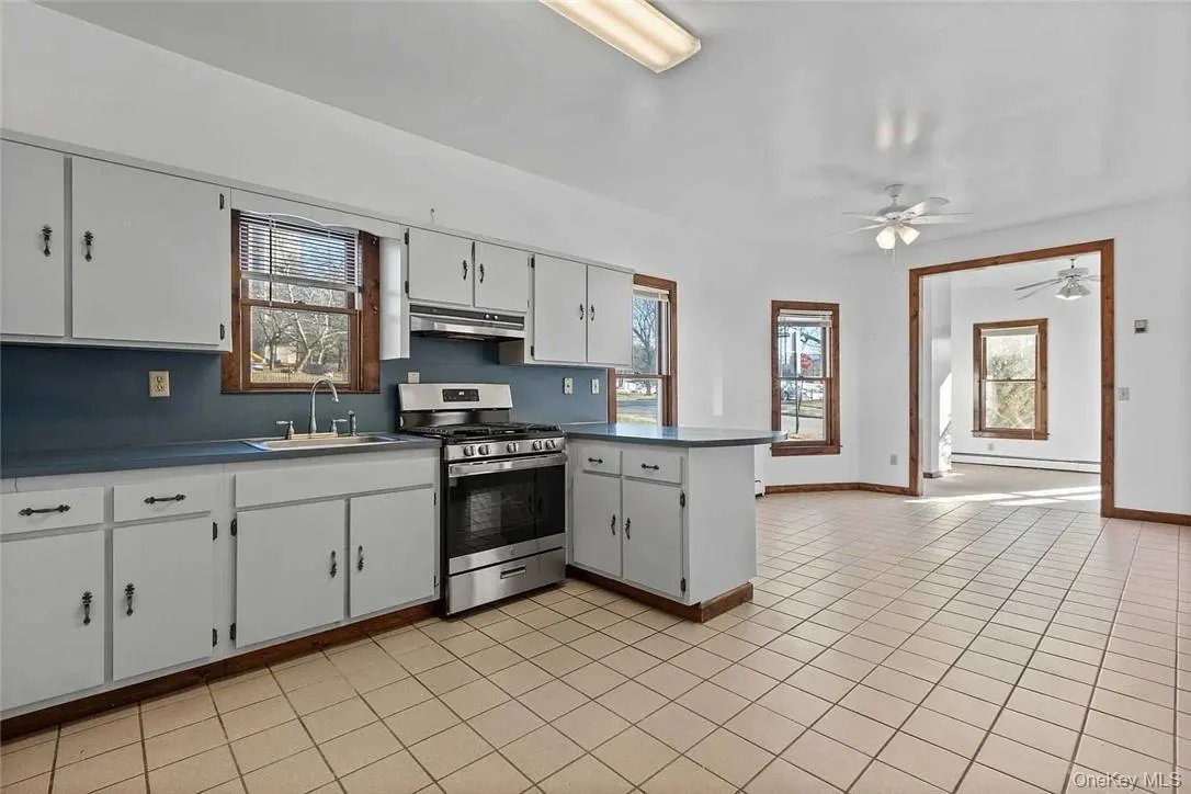 Kitchen with a peninsula, stainless steel gas range oven, white cabinets, a ceiling fan, and light tile patterned floors Kitchen with a peninsula, stainless steel gas range oven, white cabinets, a ceiling fan, and light tile patterned floors