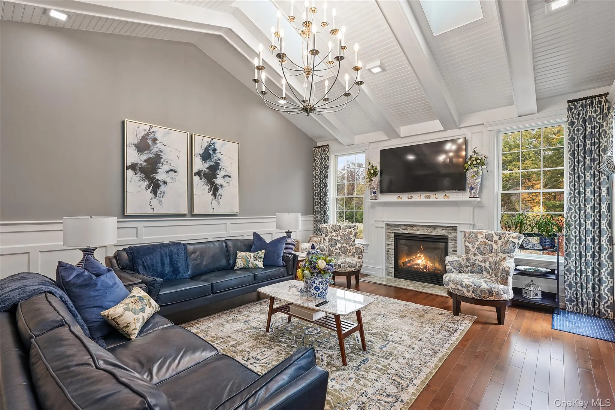 Living room featuring beam ceiling, a decorative wall, hardwood / wood-style floors, a fireplace with flush hearth, and wainscoting Living room featuring beam ceiling, a decorative wall, hardwood / wood-style floors, a fireplace with flush hearth, and wainscoting