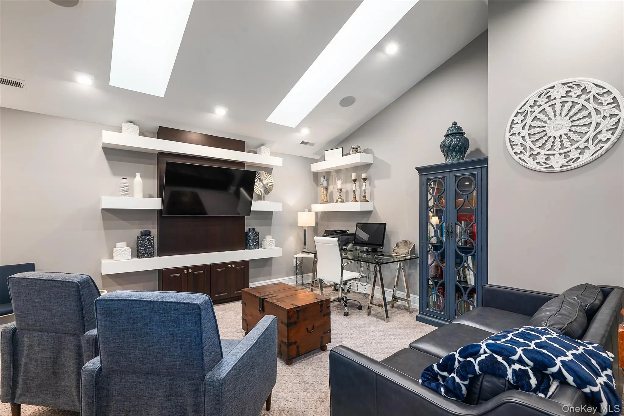 Living area with a desk, a skylight, light colored carpet, and high vaulted ceiling Living area with a desk, a skylight, light colored carpet, and high vaulted ceiling
