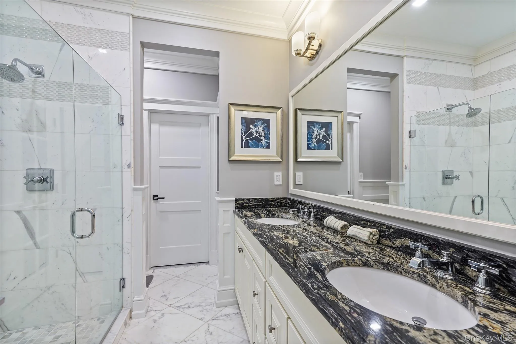 Full bath featuring light marble finish floors, double vanity, crown molding, and a marble finish shower Full bath featuring light marble finish floors, double vanity, crown molding, and a marble finish shower
