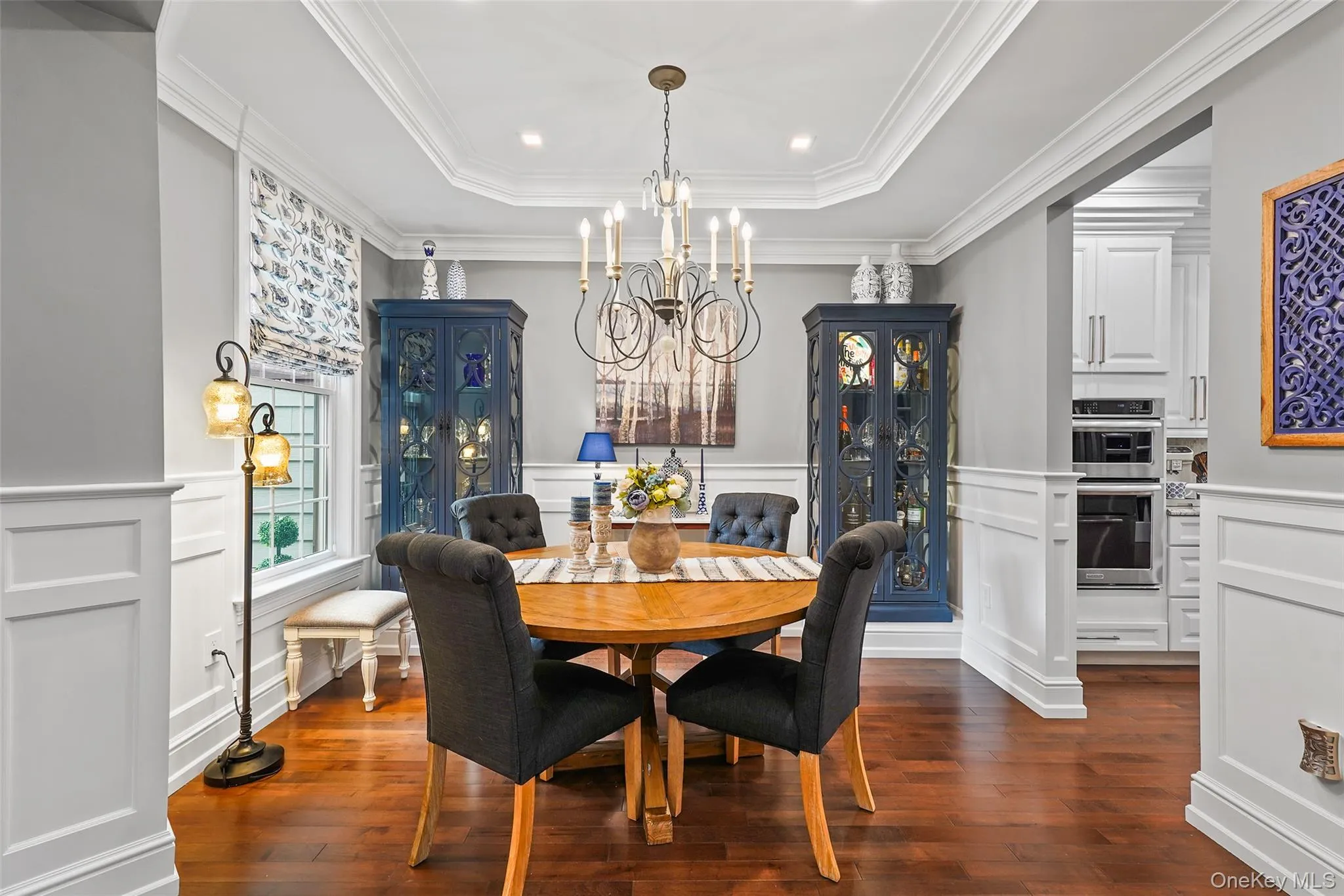 Dining area featuring dark wood-type flooring, a chandelier, a tray ceiling, a decorative wall, and ornamental molding Dining area featuring dark wood-type flooring, a chandelier, a tray ceiling, a decorative wall, and ornamental molding