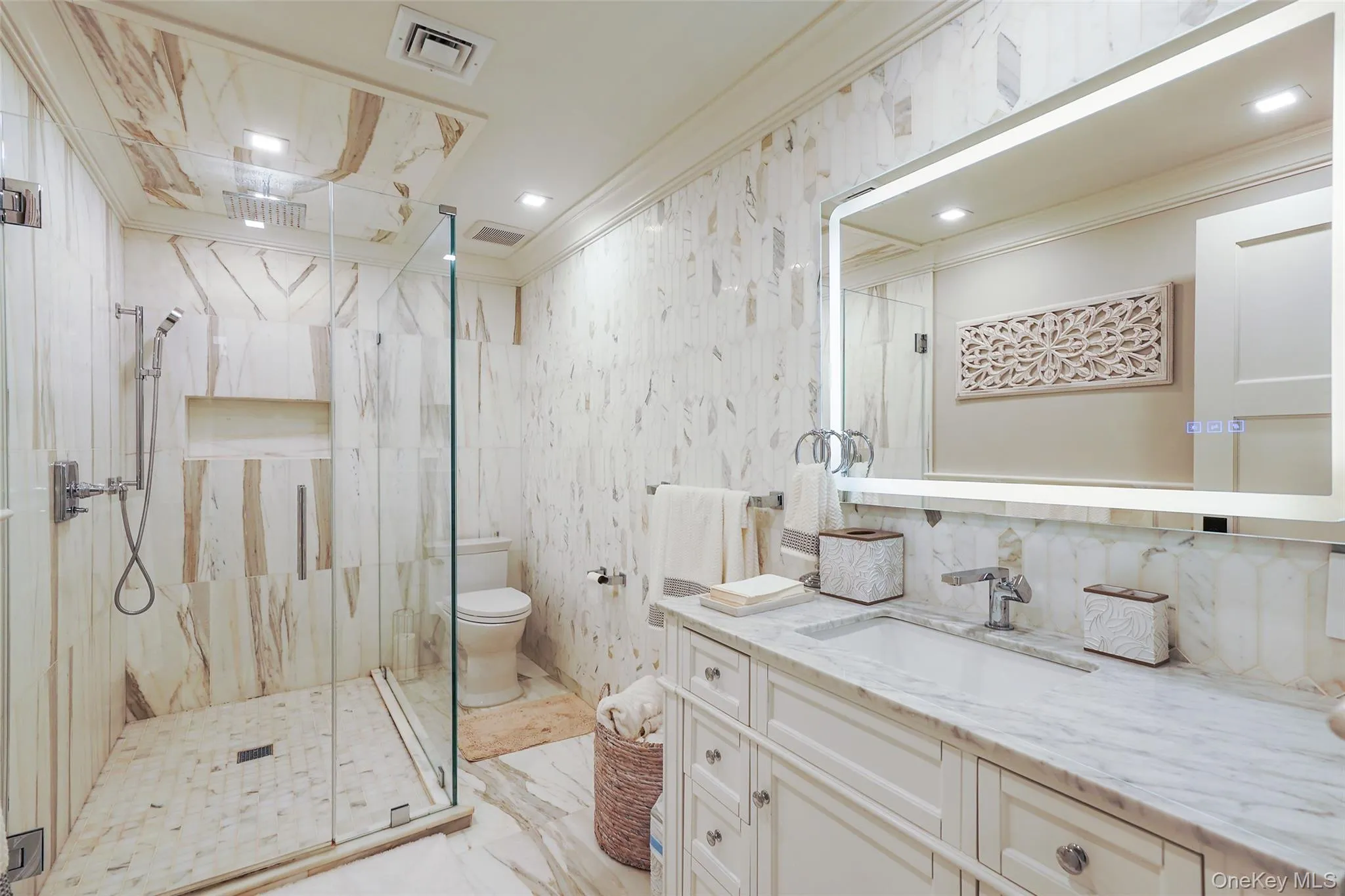 Bathroom featuring crown molding, vanity, tile walls, a marble finish shower, and light marble finish flooring Bathroom featuring crown molding, vanity, tile walls, a marble finish shower, and light marble finish flooring