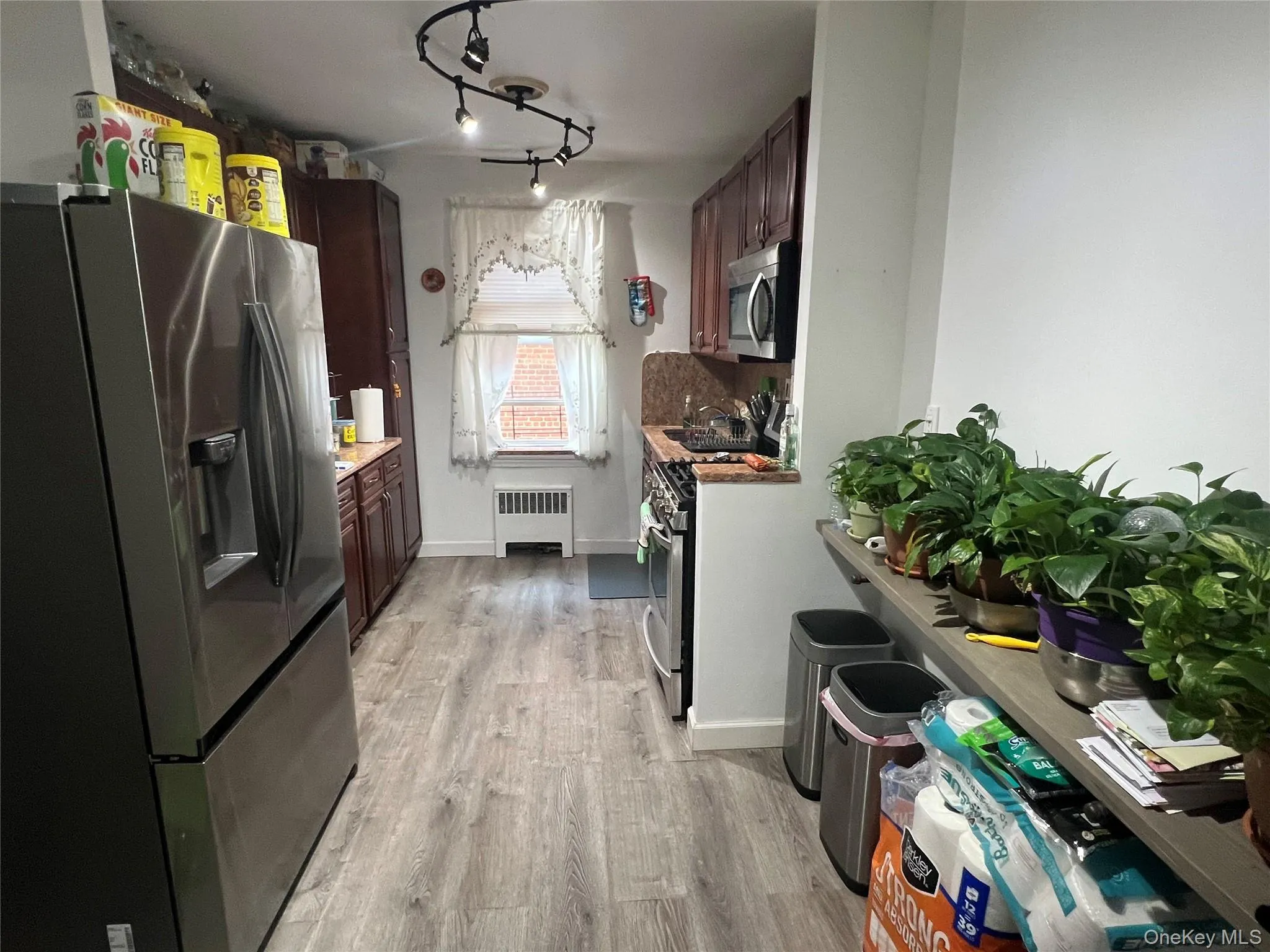 Kitchen with track lighting, baseboards, radiator, stainless steel appliances, and light wood-style flooring Kitchen with track lighting, baseboards, radiator, stainless steel appliances, and light wood-style flooring