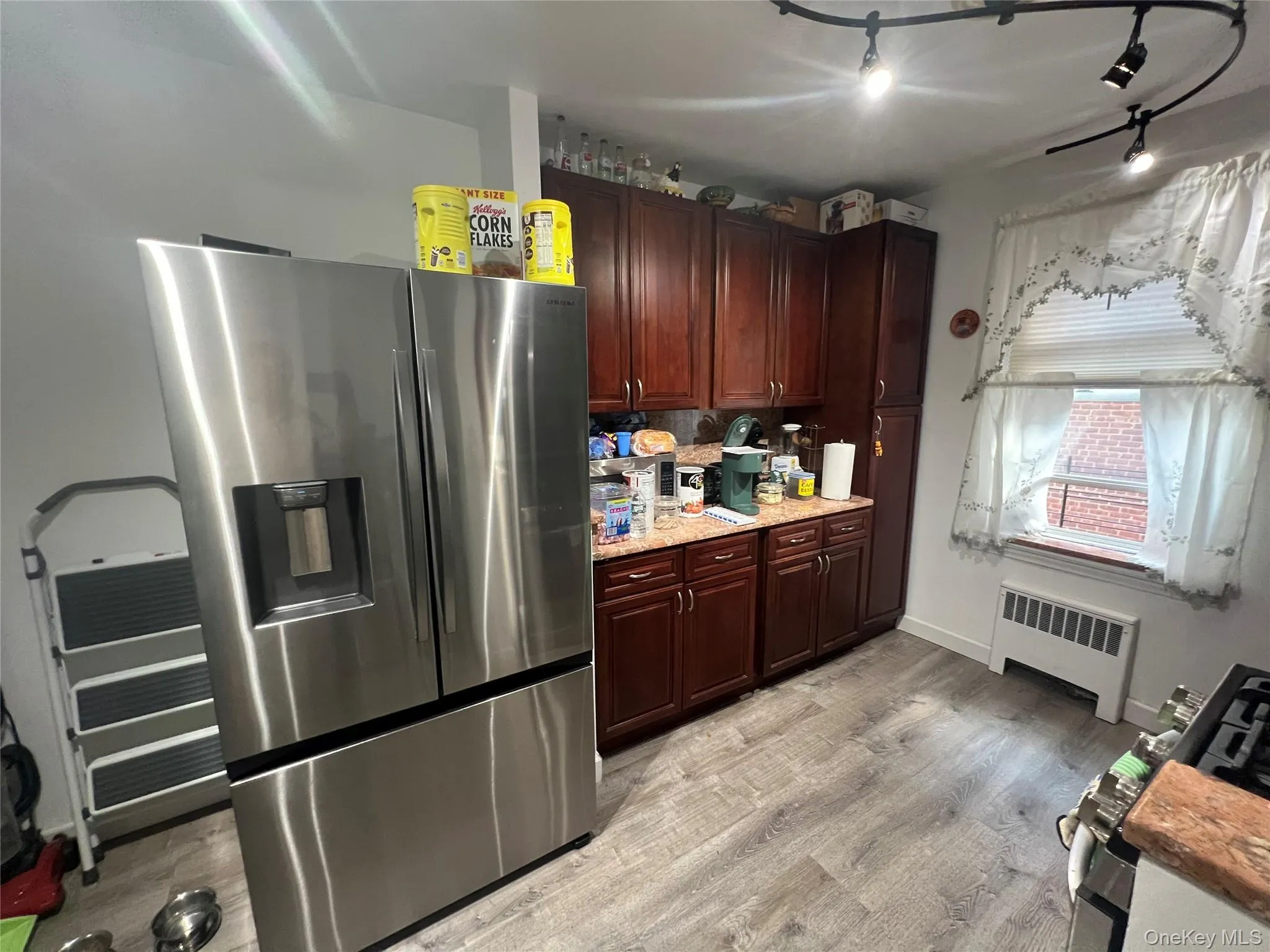 Kitchen with baseboards, light wood-style floors, stainless steel fridge, and radiator Kitchen with baseboards, light wood-style floors, stainless steel fridge, and radiator