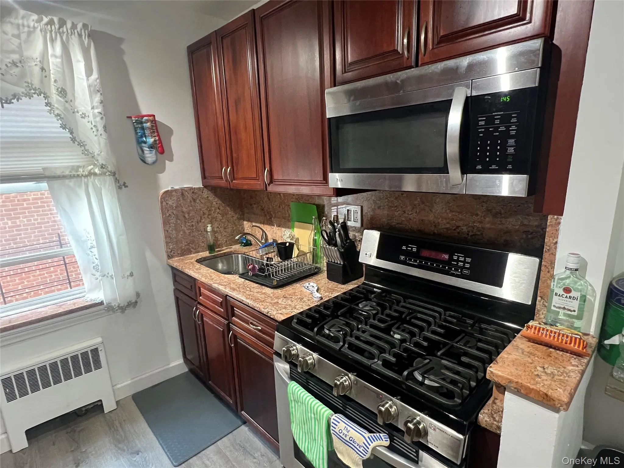 Kitchen with light wood-style floors, radiator, tasteful backsplash, appliances with stainless steel finishes, and a sink Kitchen with light wood-style floors, radiator, tasteful backsplash, appliances with stainless steel finishes, and a sink
