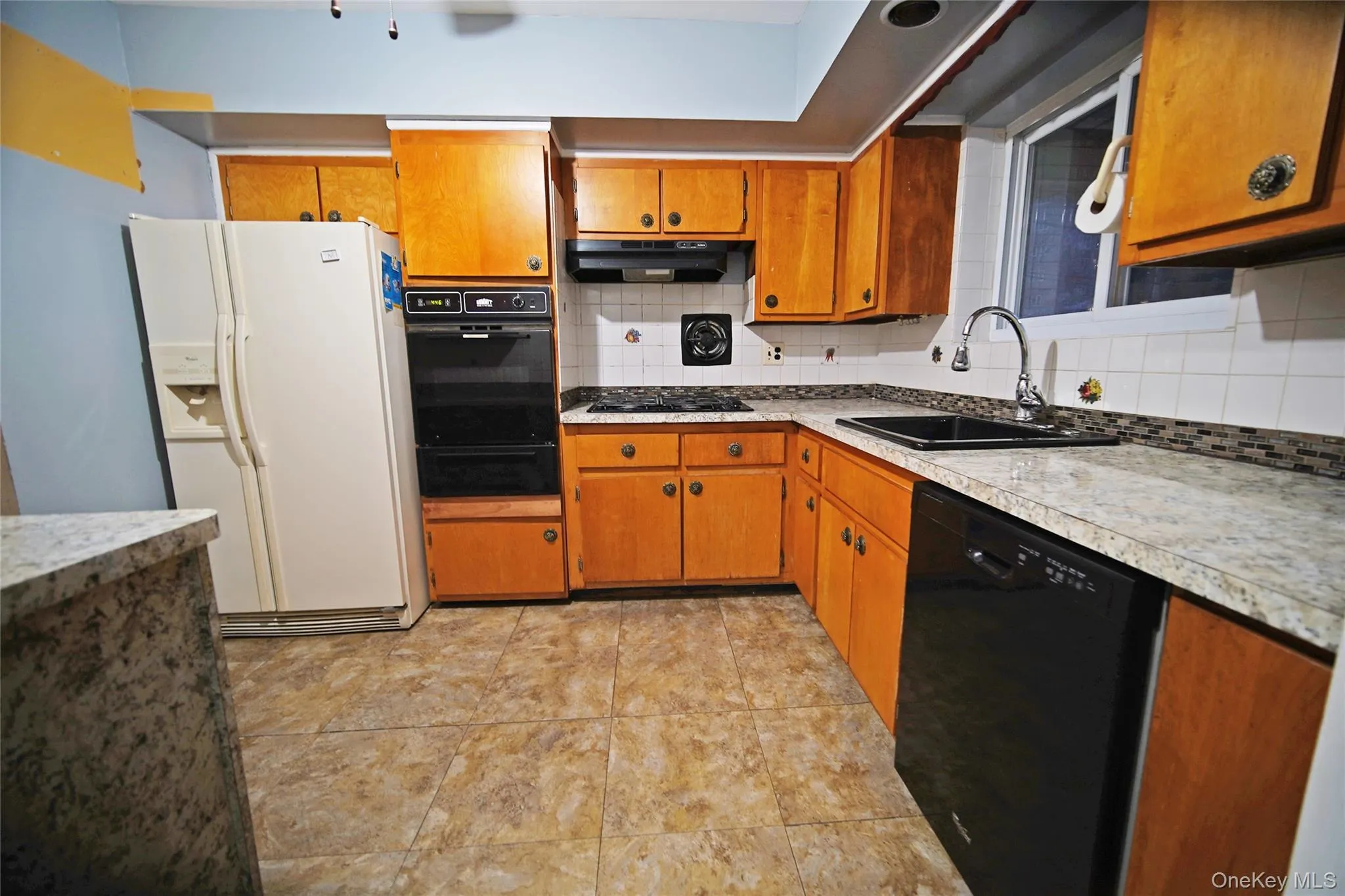 Kitchen featuring black appliances, tasteful backsplash, brown cabinetry, light countertops, and a warming drawer Kitchen featuring black appliances, tasteful backsplash, brown cabinetry, light countertops, and a warming drawer