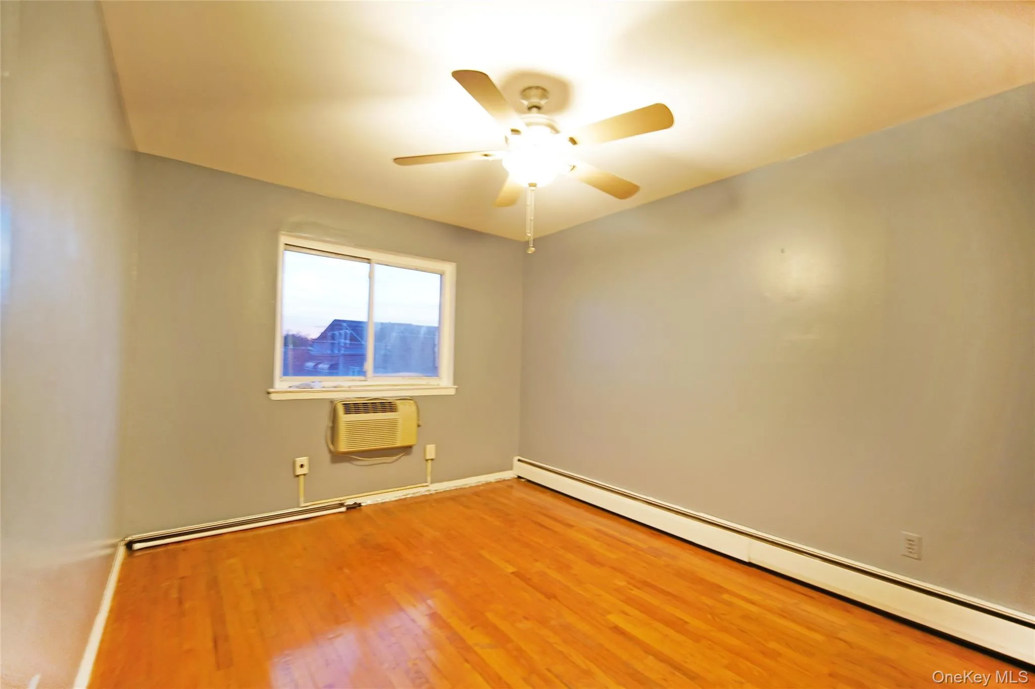 Unfurnished room featuring a baseboard heating unit, ceiling fan, light wood finished floors, and an AC wall unit Unfurnished room featuring a baseboard heating unit, ceiling fan, light wood finished floors, and an AC wall unit