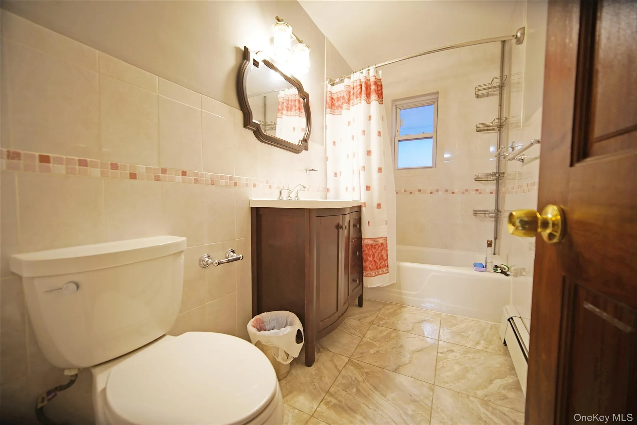 Full bathroom featuring vanity, shower / bath combo, a baseboard radiator, tile walls, and light marble finish flooring Full bathroom featuring vanity, shower / bath combo, a baseboard radiator, tile walls, and light marble finish flooring