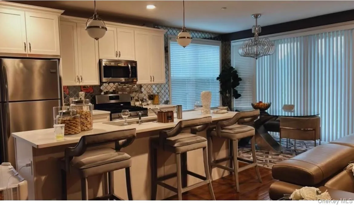 Kitchen featuring stainless steel appliances, hanging light fixtures, a breakfast bar area, and white cabinets Kitchen featuring stainless steel appliances, hanging light fixtures, a breakfast bar area, and white cabinets