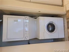 Washroom featuring stacked washing machine and dryer and light tile patterned floors Washroom featuring stacked washing machine and dryer and light tile patterned floors