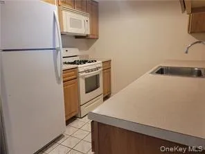 Kitchen with white appliances, light countertops, light tile patterned flooring, and brown cabinetry Kitchen with white appliances, light countertops, light tile patterned flooring, and brown cabinetry