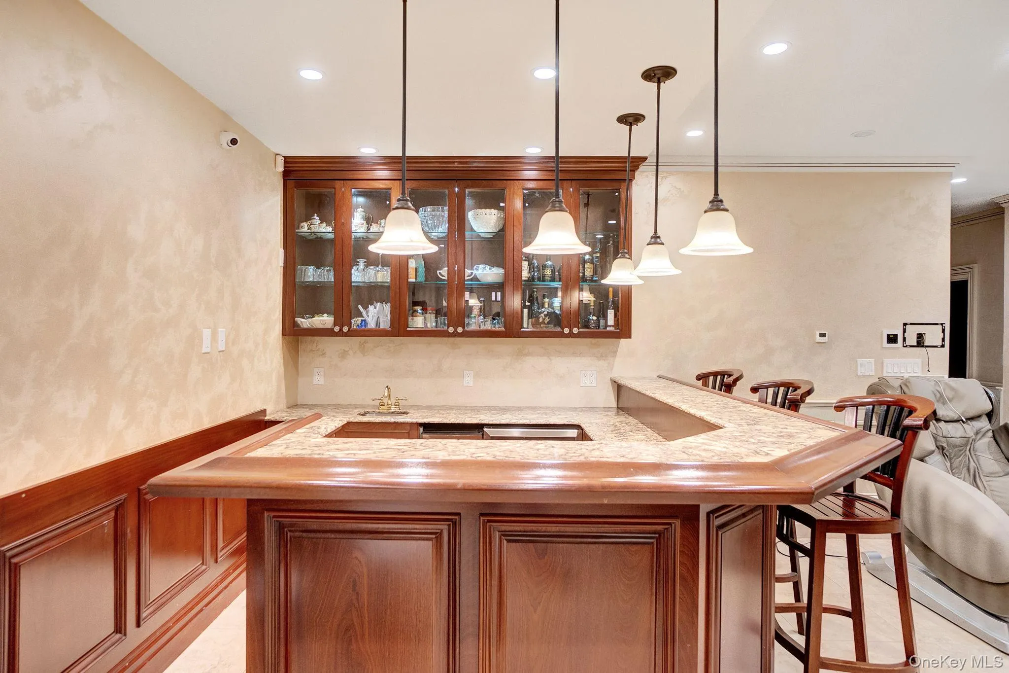 Indoor wet bar featuring glass insert cabinets, pendant lighting, light stone counters, recessed lighting, and brown cabinets Indoor wet bar featuring glass insert cabinets, pendant lighting, light stone counters, recessed lighting, and brown cabinets