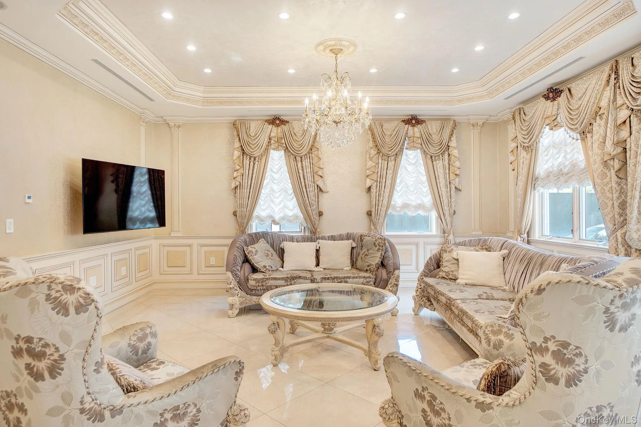 Living area featuring a decorative wall, crown molding, a wainscoted wall, a raised ceiling, and a chandelier Living area featuring a decorative wall, crown molding, a wainscoted wall, a raised ceiling, and a chandelier