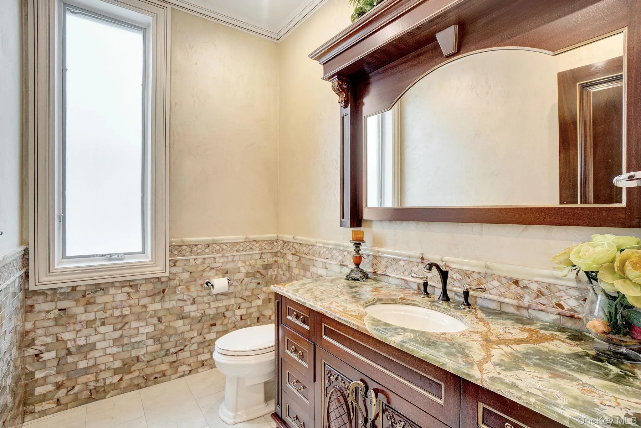 Bathroom with vanity, tile walls, light tile patterned floors, a wainscoted wall, and ornamental molding Bathroom with vanity, tile walls, light tile patterned floors, a wainscoted wall, and ornamental molding