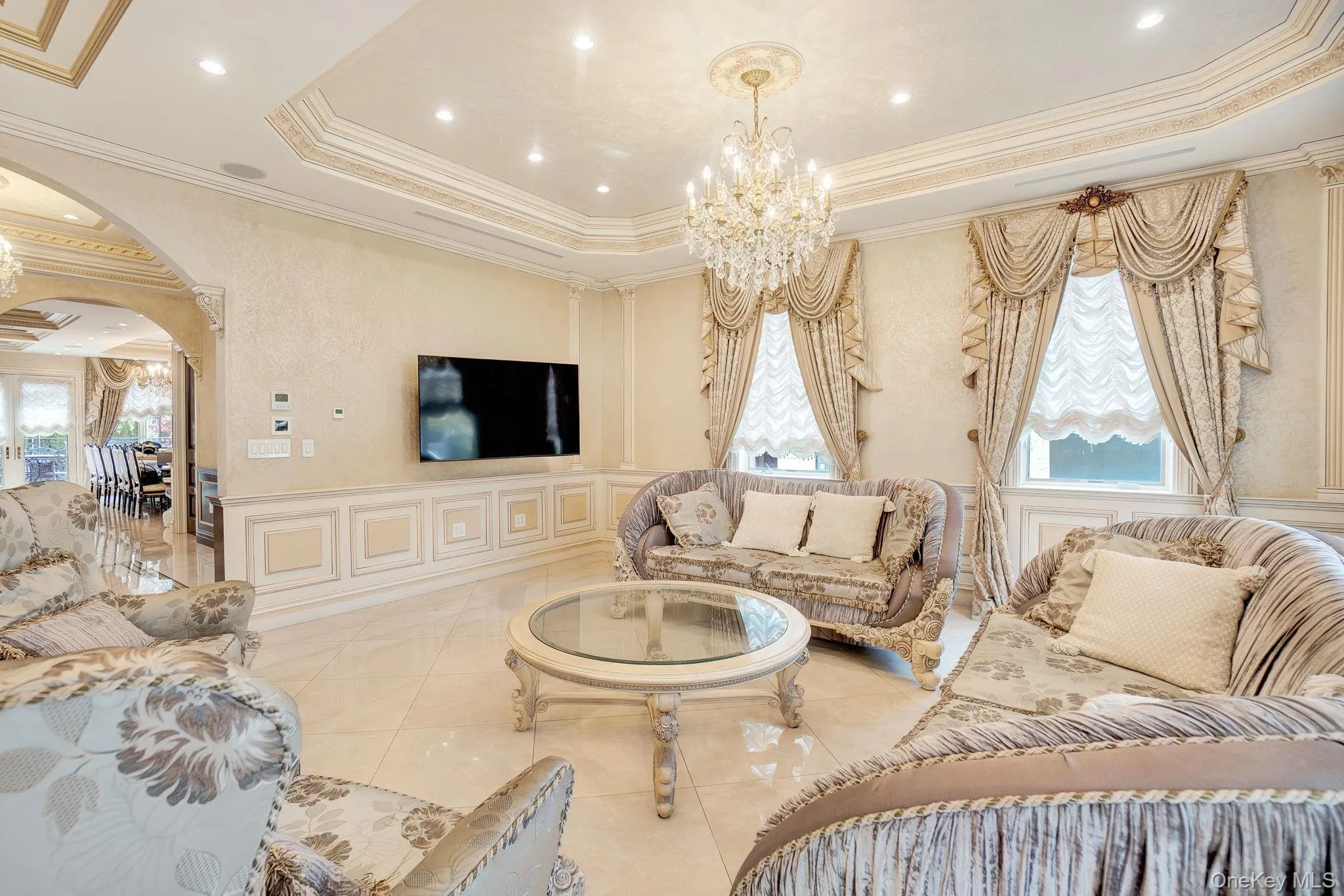 Living room featuring a chandelier, arched walkways, crown molding, a raised ceiling, and a decorative wall Living room featuring a chandelier, arched walkways, crown molding, a raised ceiling, and a decorative wall