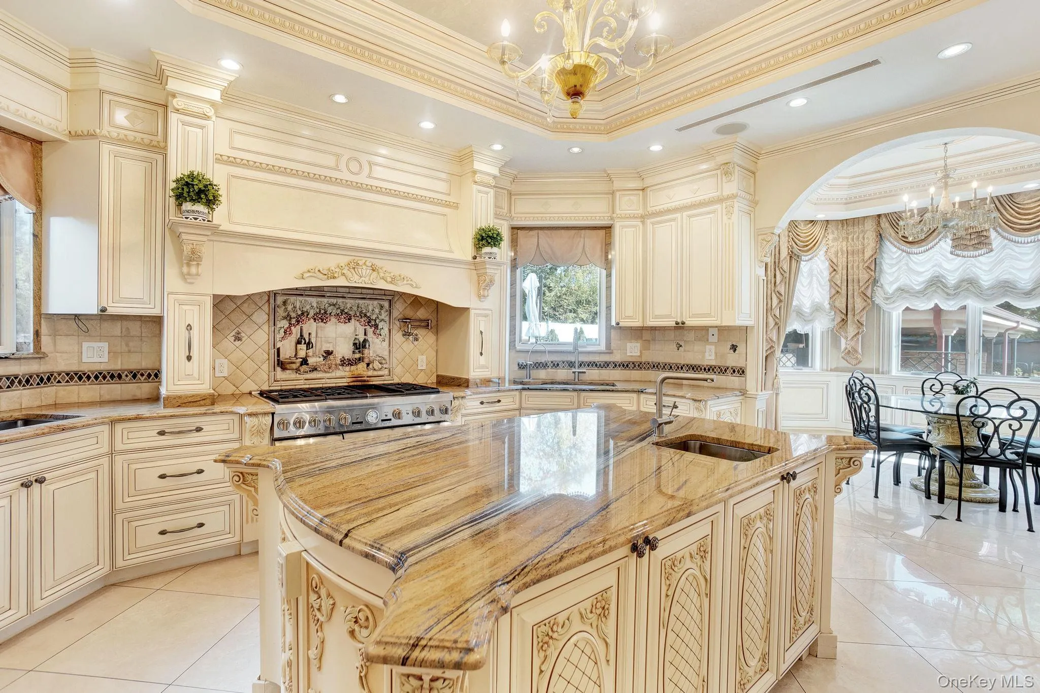 Kitchen with cream cabinetry, a chandelier, ornamental molding, light stone counters, and backsplash Kitchen with cream cabinetry, a chandelier, ornamental molding, light stone counters, and backsplash