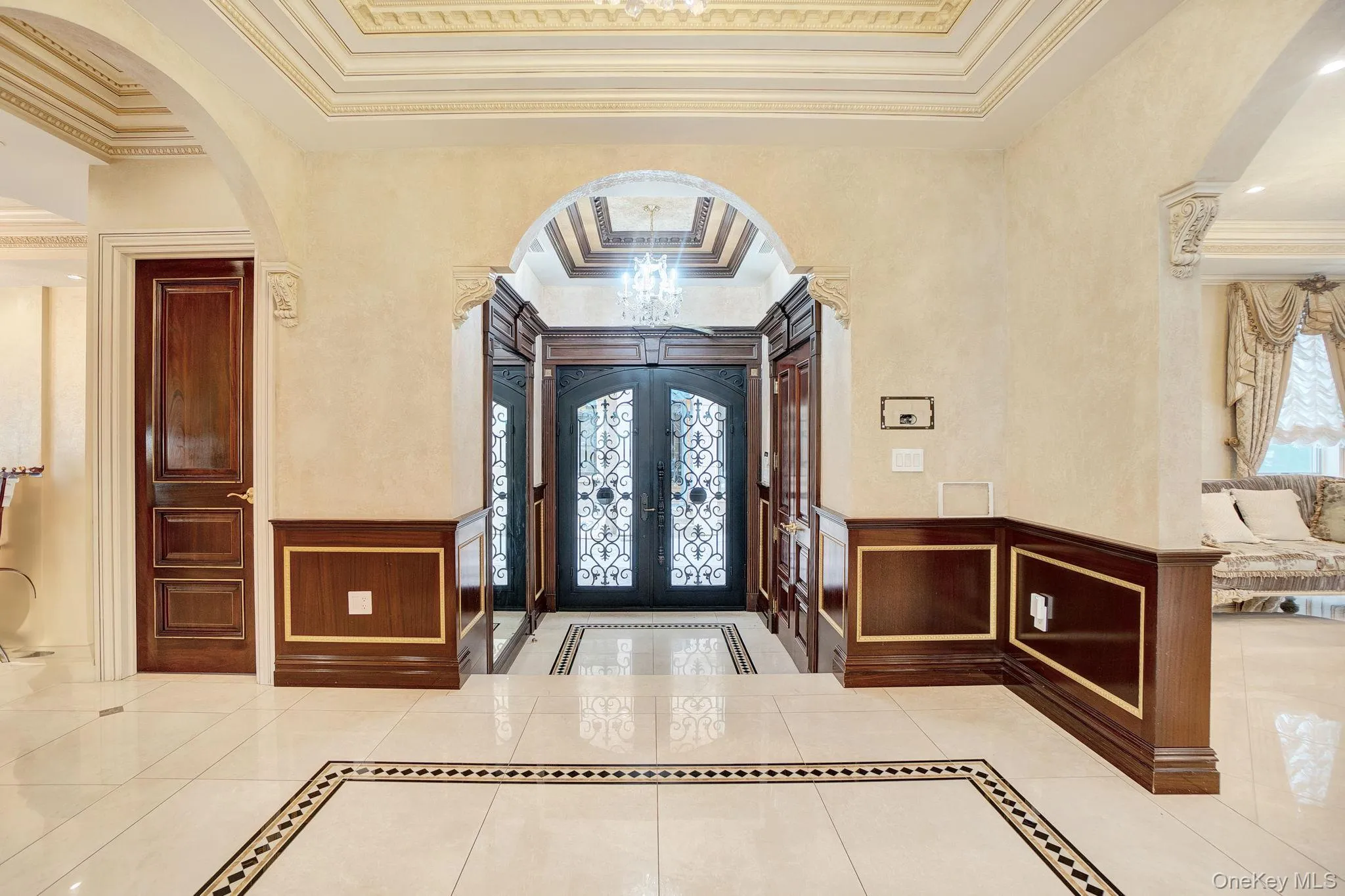 Foyer featuring arched walkways, inlaid floor details, crown molding, a wainscoted wall, and a decorative wall Foyer featuring arched walkways, inlaid floor details, crown molding, a wainscoted wall, and a decorative wall