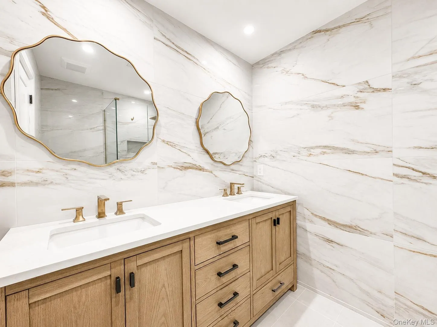 Dual vanity featuring light wood-finish cabinetry with black hardware, white countertops, and integrated sinks Dual vanity featuring light wood-finish cabinetry with black hardware, white countertops, and integrated sinks