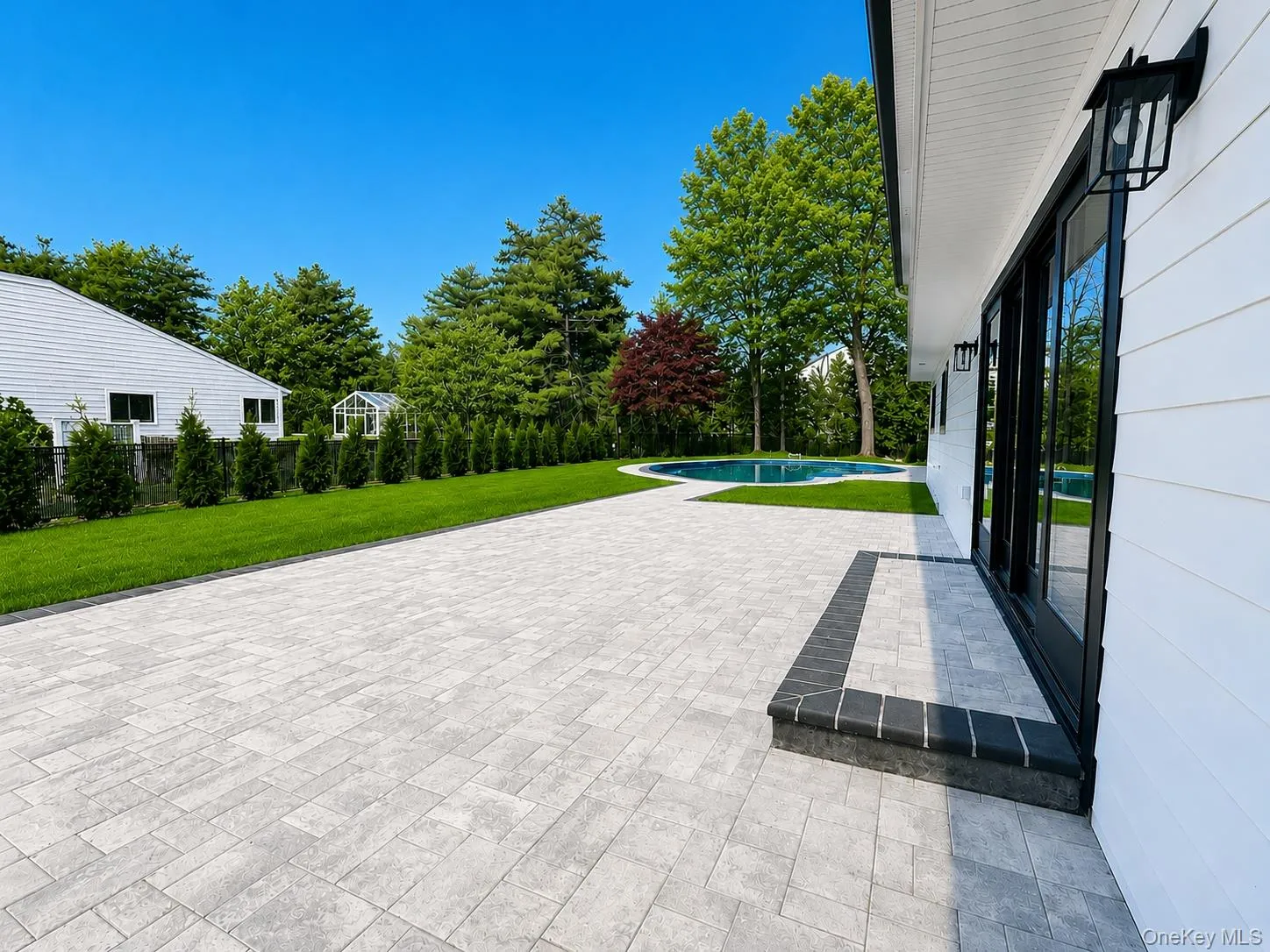 Expansive paver patio with a contrasting border, leading to a manicured lawn and a curved inground pool Expansive paver patio with a contrasting border, leading to a manicured lawn and a curved inground pool