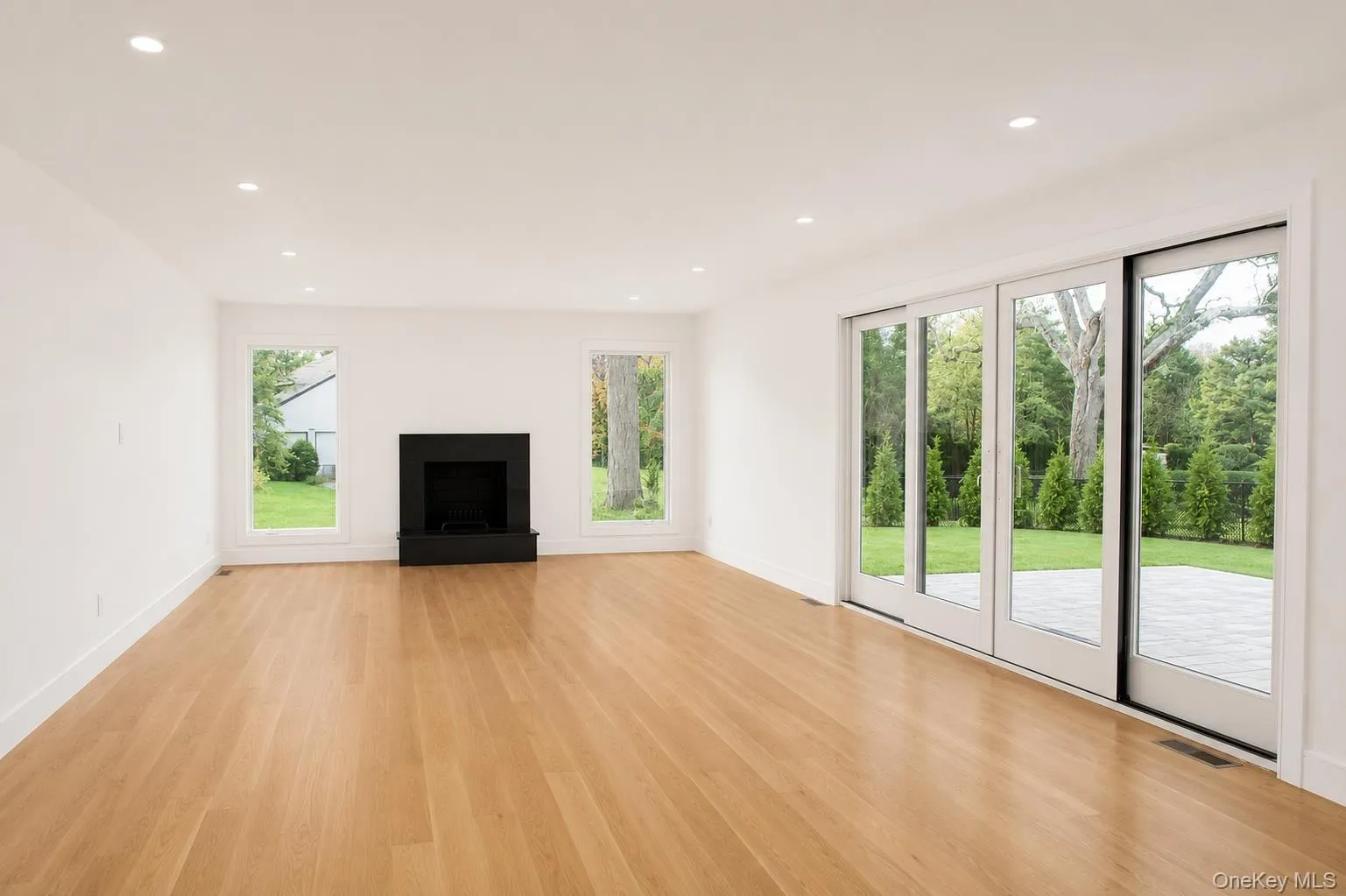 Spacious room featuring light wood-finish flooring, a modern black fireplace, and recessed ceiling lighting Spacious room featuring light wood-finish flooring, a modern black fireplace, and recessed ceiling lighting