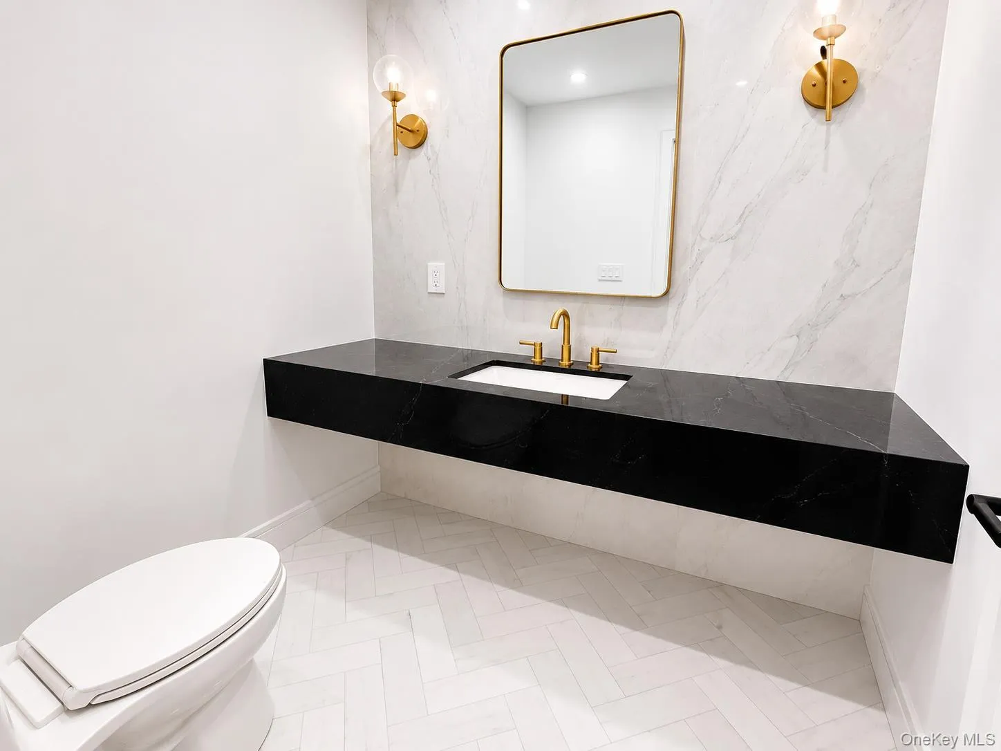 Floating black vanity with an integrated sink and brass faucet, complemented by a rectangular mirror with a brass frame and coordinating wall sconces Floating black vanity with an integrated sink and brass faucet, complemented by a rectangular mirror with a brass frame and coordinating wall sconces
