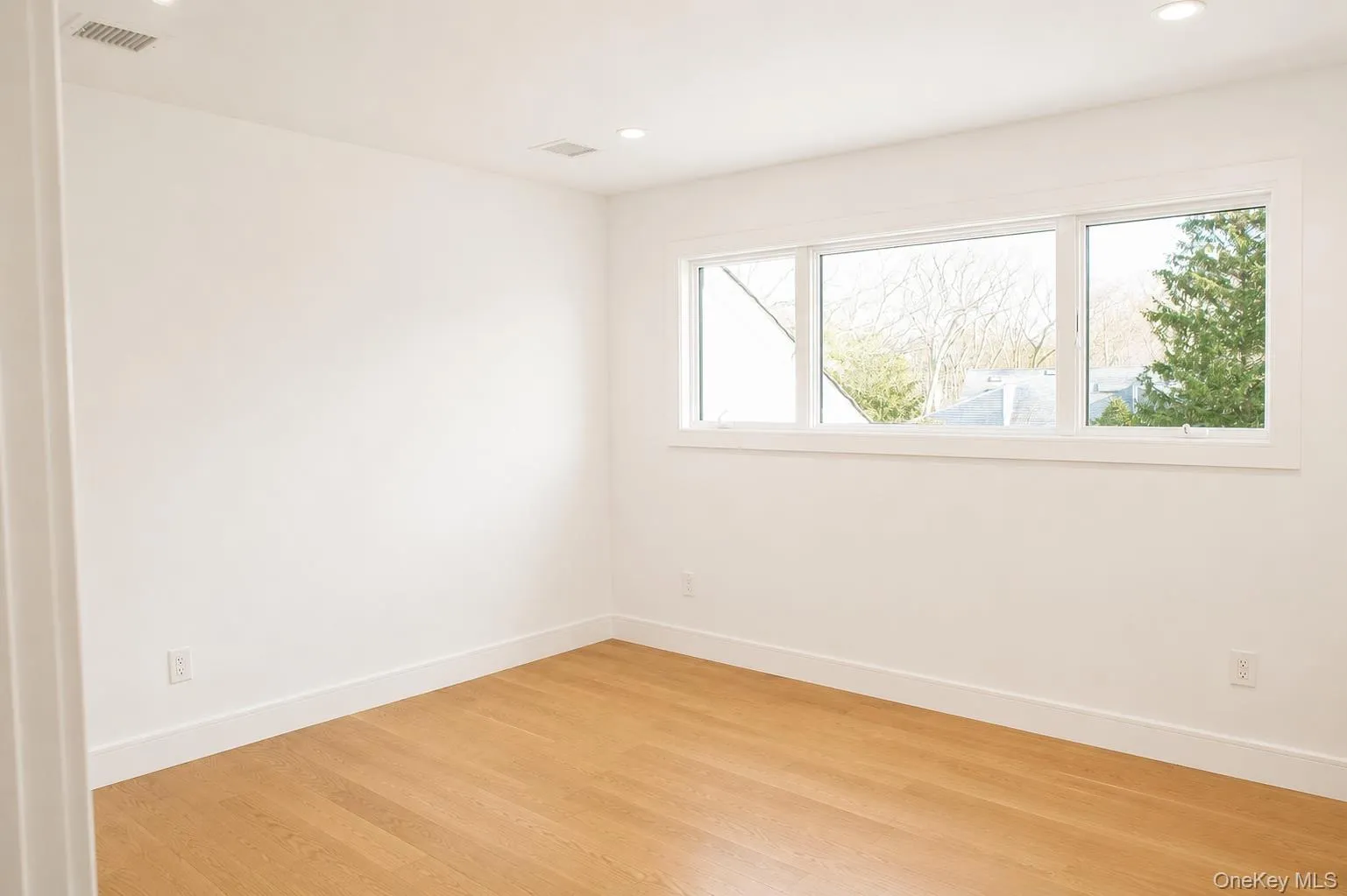 Bright room featuring a multi-pane window, wood-finish flooring, recessed lighting, white walls, and a flat ceiling Bright room featuring a multi-pane window, wood-finish flooring, recessed lighting, white walls, and a flat ceiling