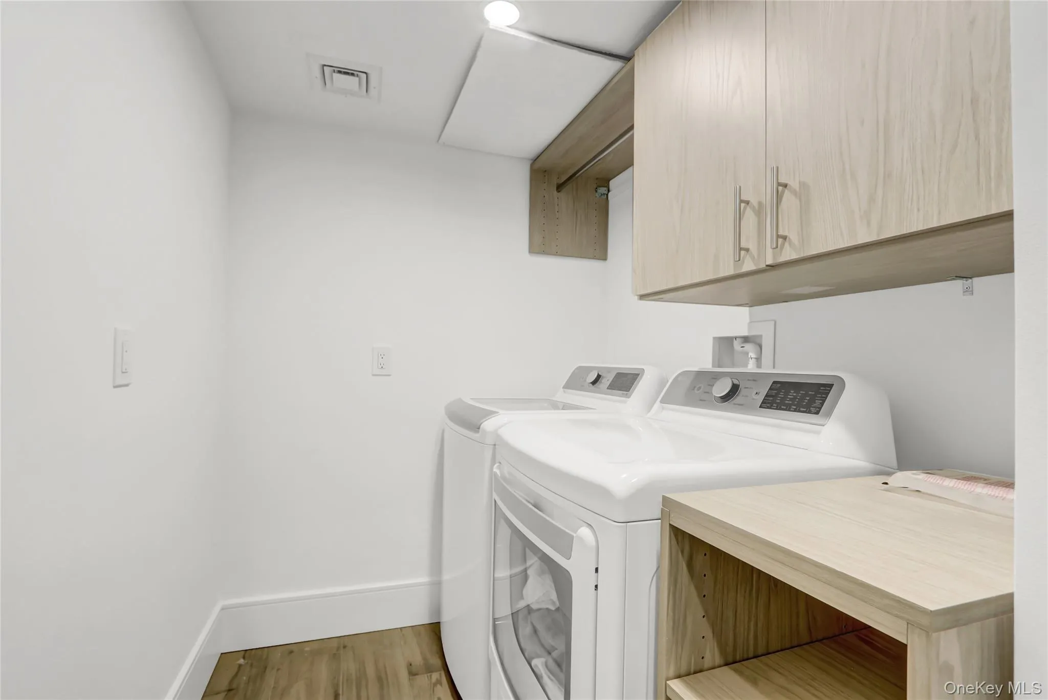 Washroom with light wood-type flooring, cabinet space, and washing machine and clothes dryer Washroom with light wood-type flooring, cabinet space, and washing machine and clothes dryer