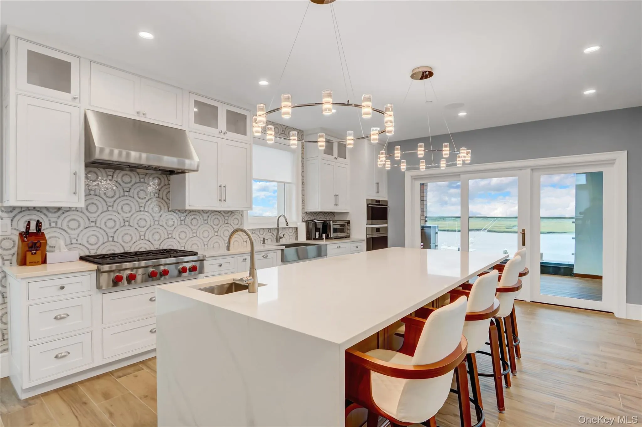 Kitchen with tasteful backsplash, glass insert cabinets, white cabinets, light wood-style flooring, and under cabinet range hood Kitchen with tasteful backsplash, glass insert cabinets, white cabinets, light wood-style flooring, and under cabinet range hood