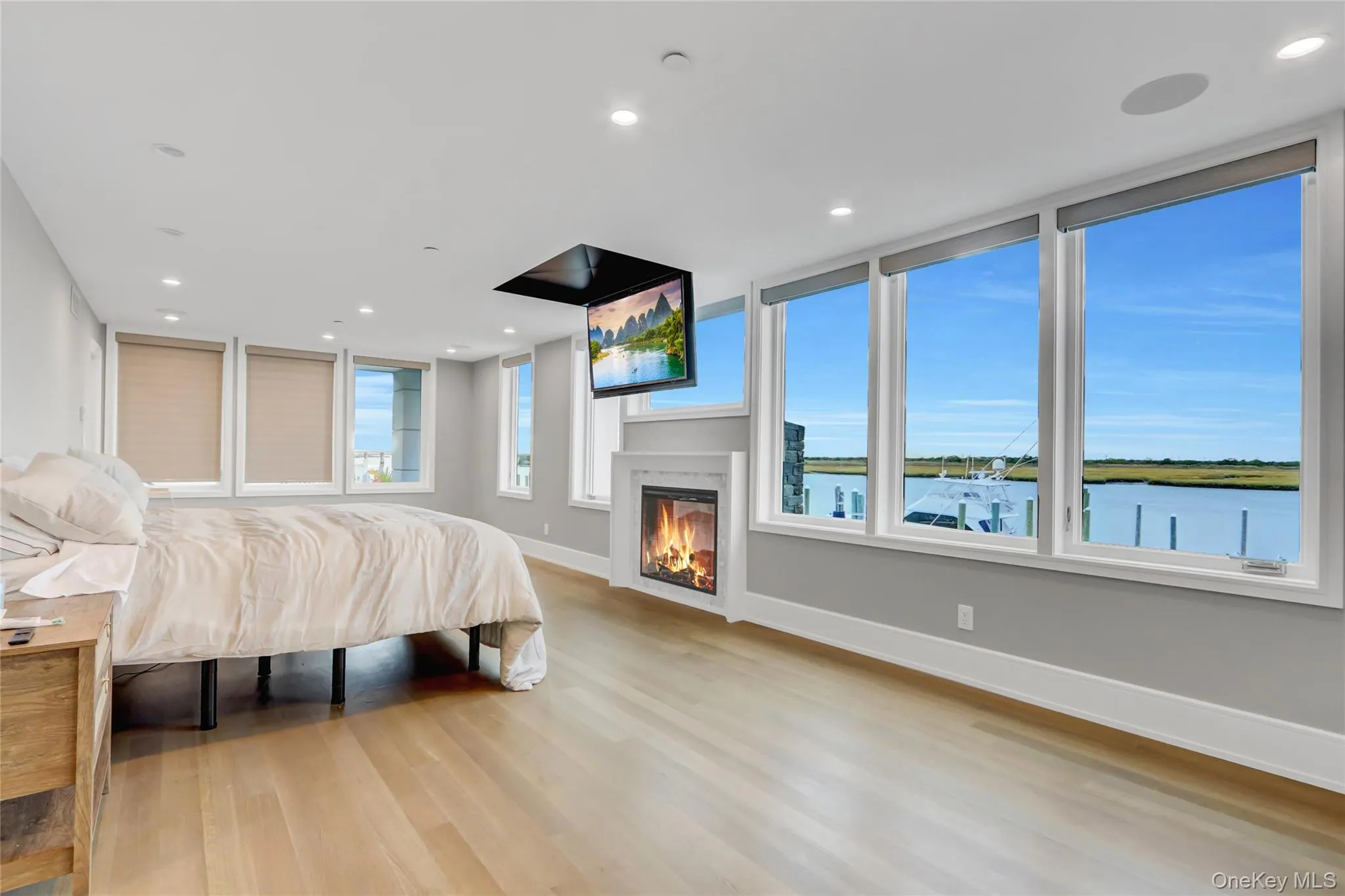 Bedroom featuring light wood-style flooring, a glass covered fireplace, and recessed lighting Bedroom featuring light wood-style flooring, a glass covered fireplace, and recessed lighting