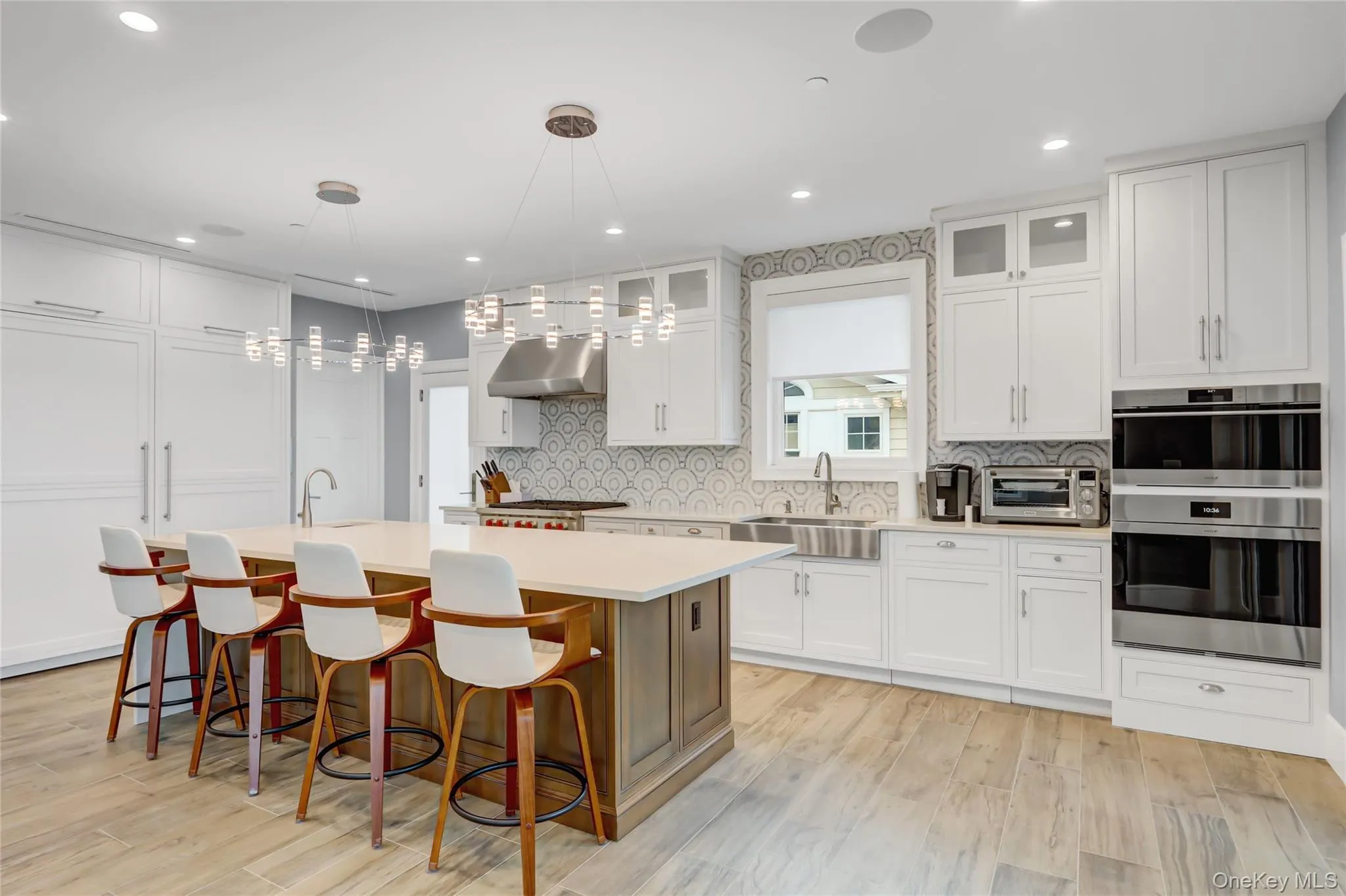 Kitchen with decorative backsplash, white cabinets, a center island with sink, glass insert cabinets, and double oven Kitchen with decorative backsplash, white cabinets, a center island with sink, glass insert cabinets, and double oven