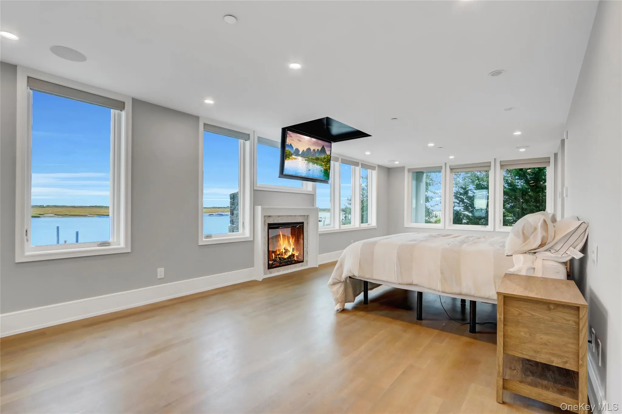 Bedroom with light wood-style flooring, a glass covered fireplace, and recessed lighting Bedroom with light wood-style flooring, a glass covered fireplace, and recessed lighting