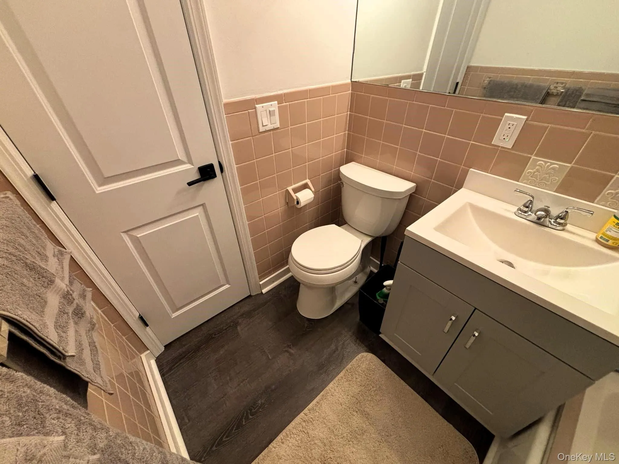 Bathroom with vanity, dark wood-style floors, tile walls, and a wainscoted wall Bathroom with vanity, dark wood-style floors, tile walls, and a wainscoted wall