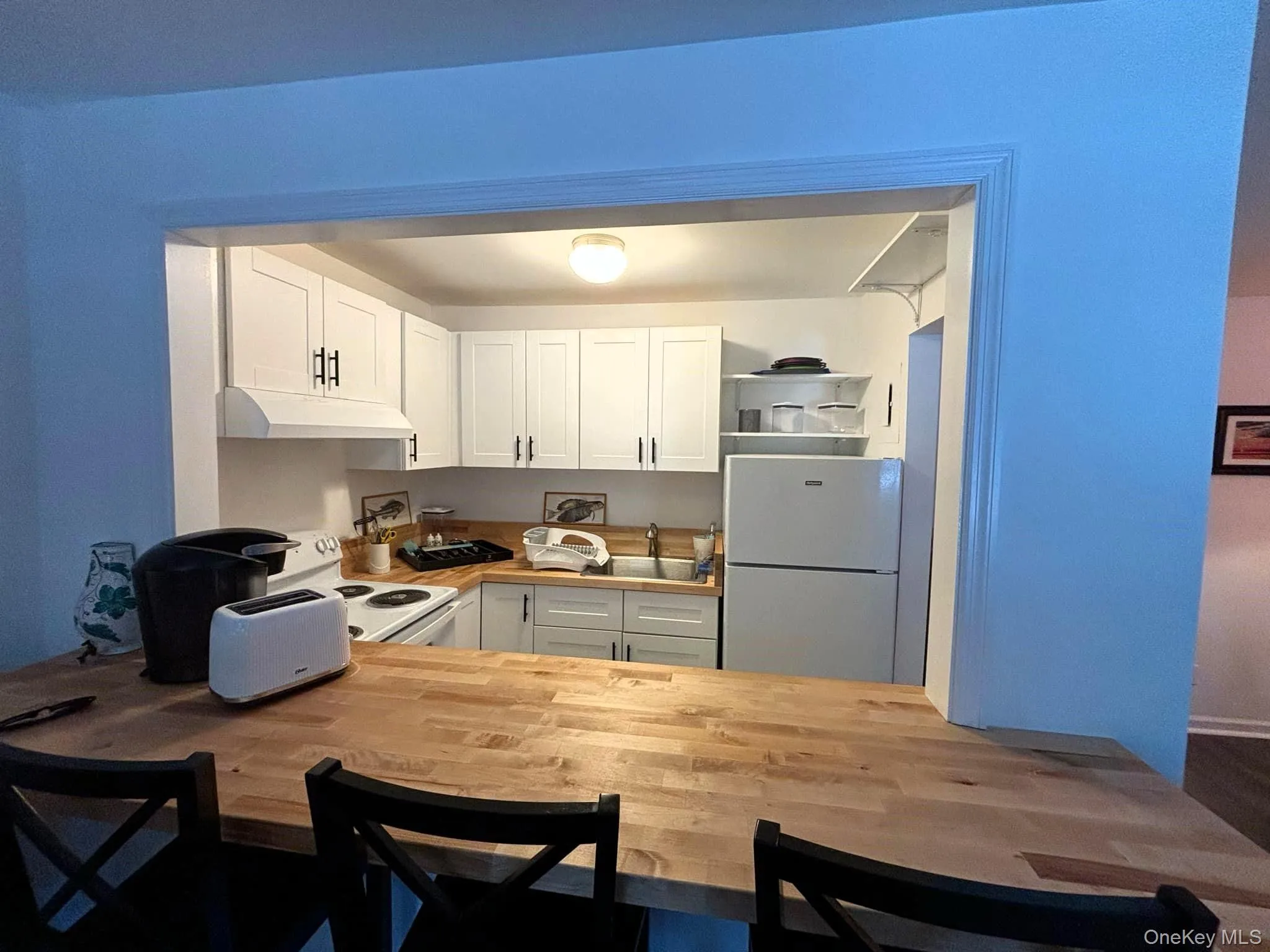 Kitchen with white cabinetry, white appliances, wood counters, under cabinet range hood, and dark wood finished floors Kitchen with white cabinetry, white appliances, wood counters, under cabinet range hood, and dark wood finished floors