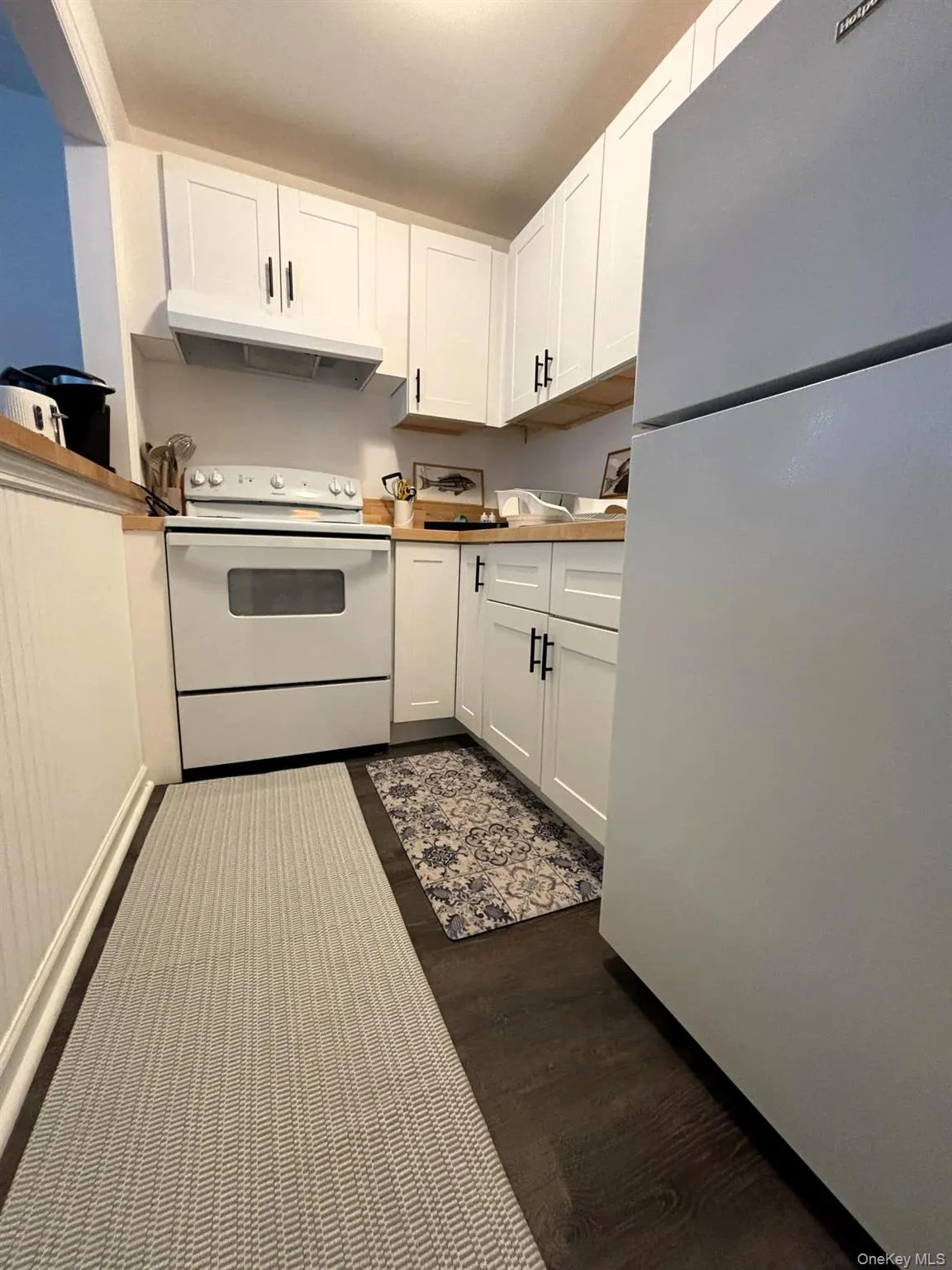 Kitchen featuring white appliances, white cabinets, under cabinet range hood, and dark wood finished floors Kitchen featuring white appliances, white cabinets, under cabinet range hood, and dark wood finished floors