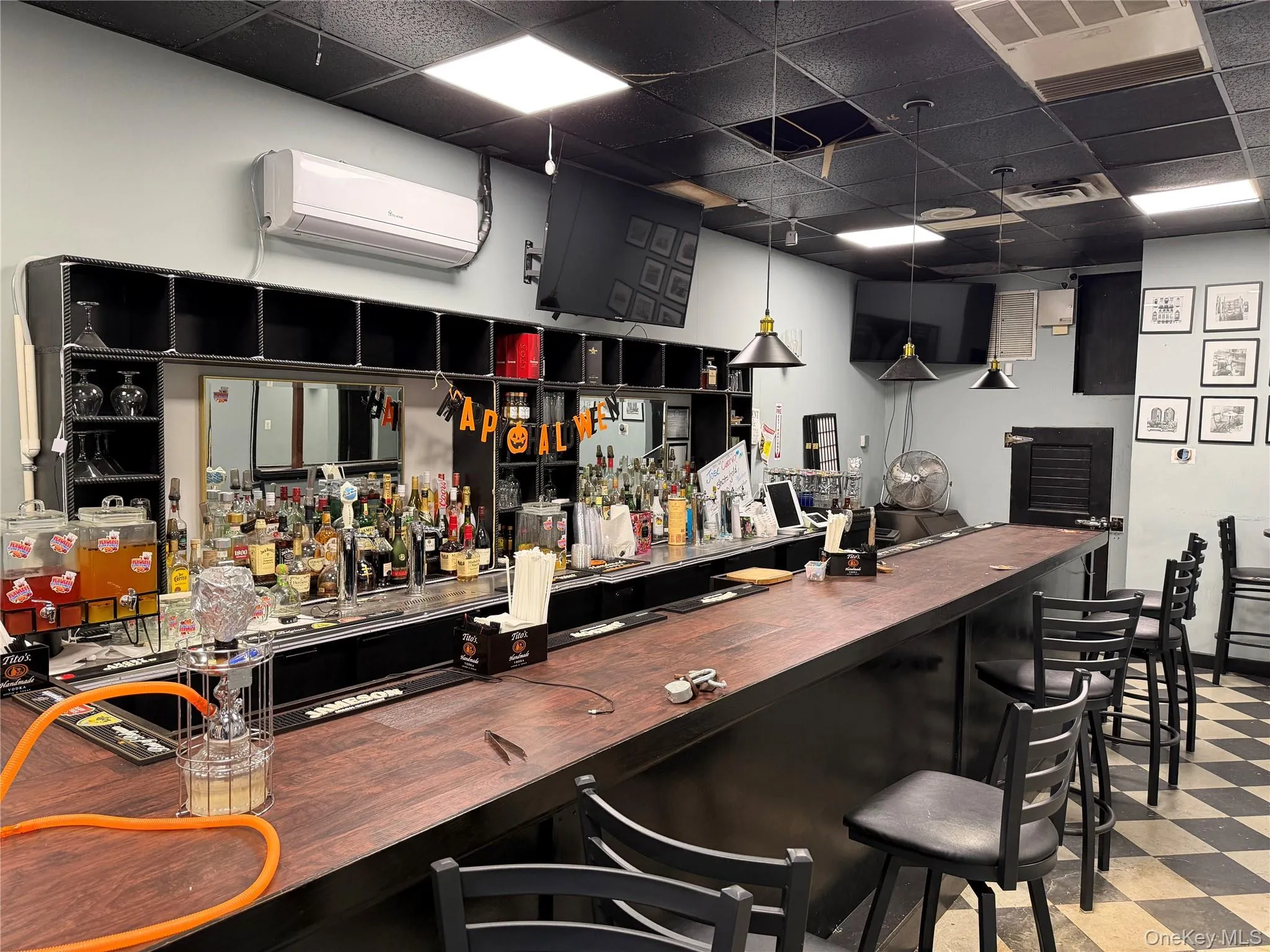 Indoor dry bar with a paneled ceiling, wood counters, a wall mounted air conditioner, dark cabinetry, and decorative light fixtures Indoor dry bar with a paneled ceiling, wood counters, a wall mounted air conditioner, dark cabinetry, and decorative light fixtures
