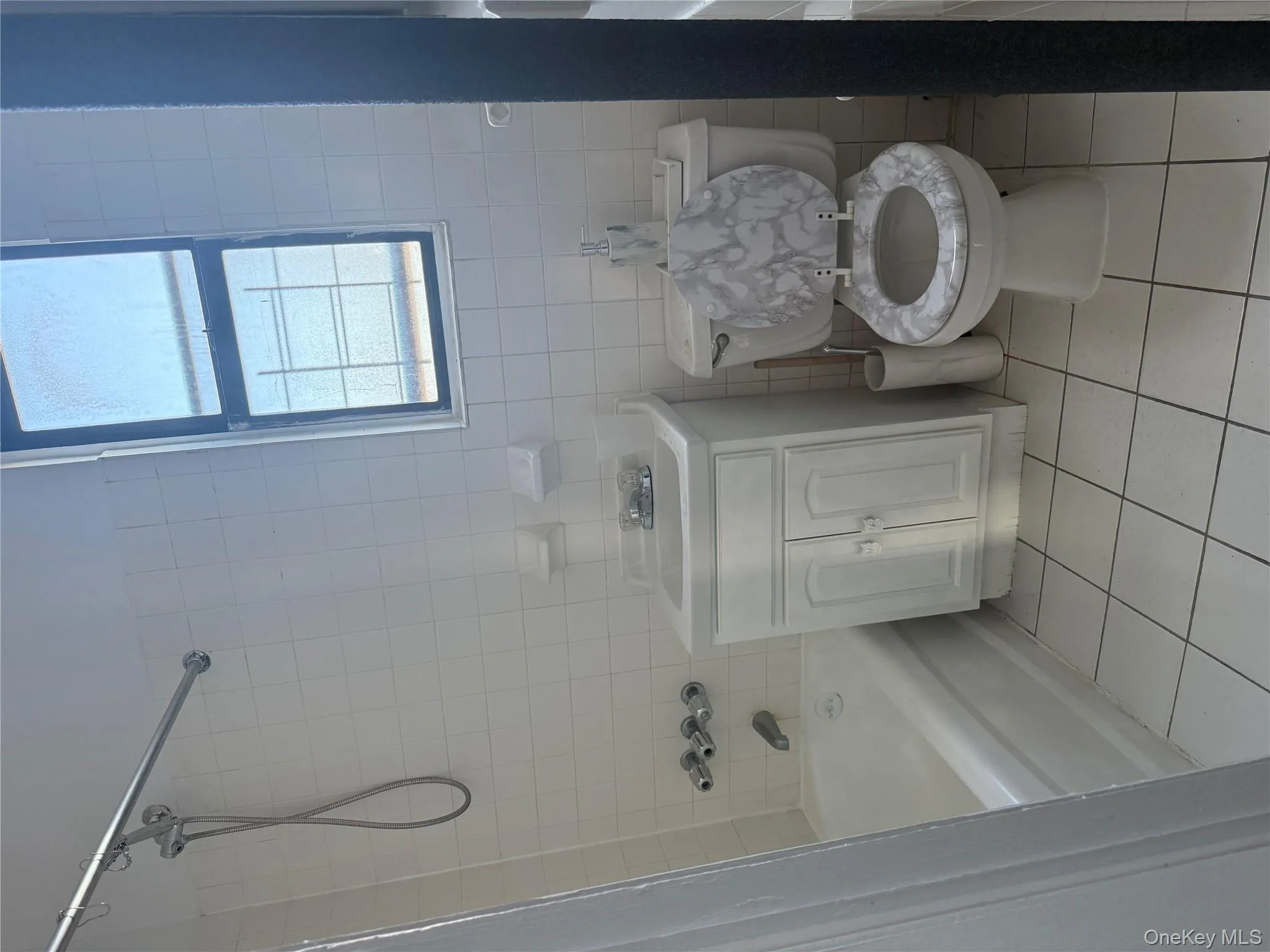 Bathroom with light tile patterned floors, tile walls, vanity, and bathtub / shower combination Bathroom with light tile patterned floors, tile walls, vanity, and bathtub / shower combination