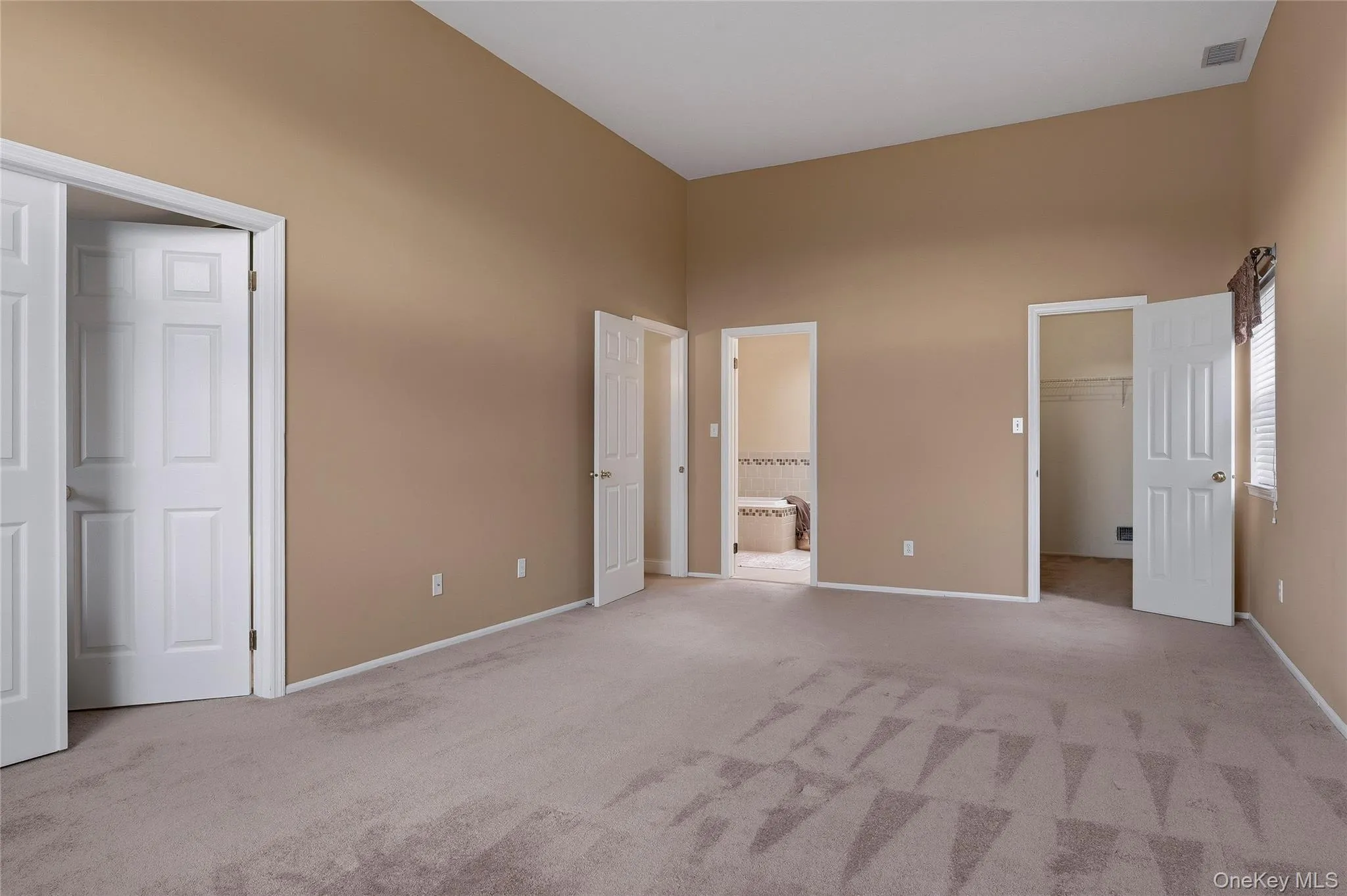 Unfurnished bedroom with light carpet, a spacious closet, a towering ceiling, and ensuite bathroom Unfurnished bedroom with light carpet, a spacious closet, a towering ceiling, and ensuite bathroom