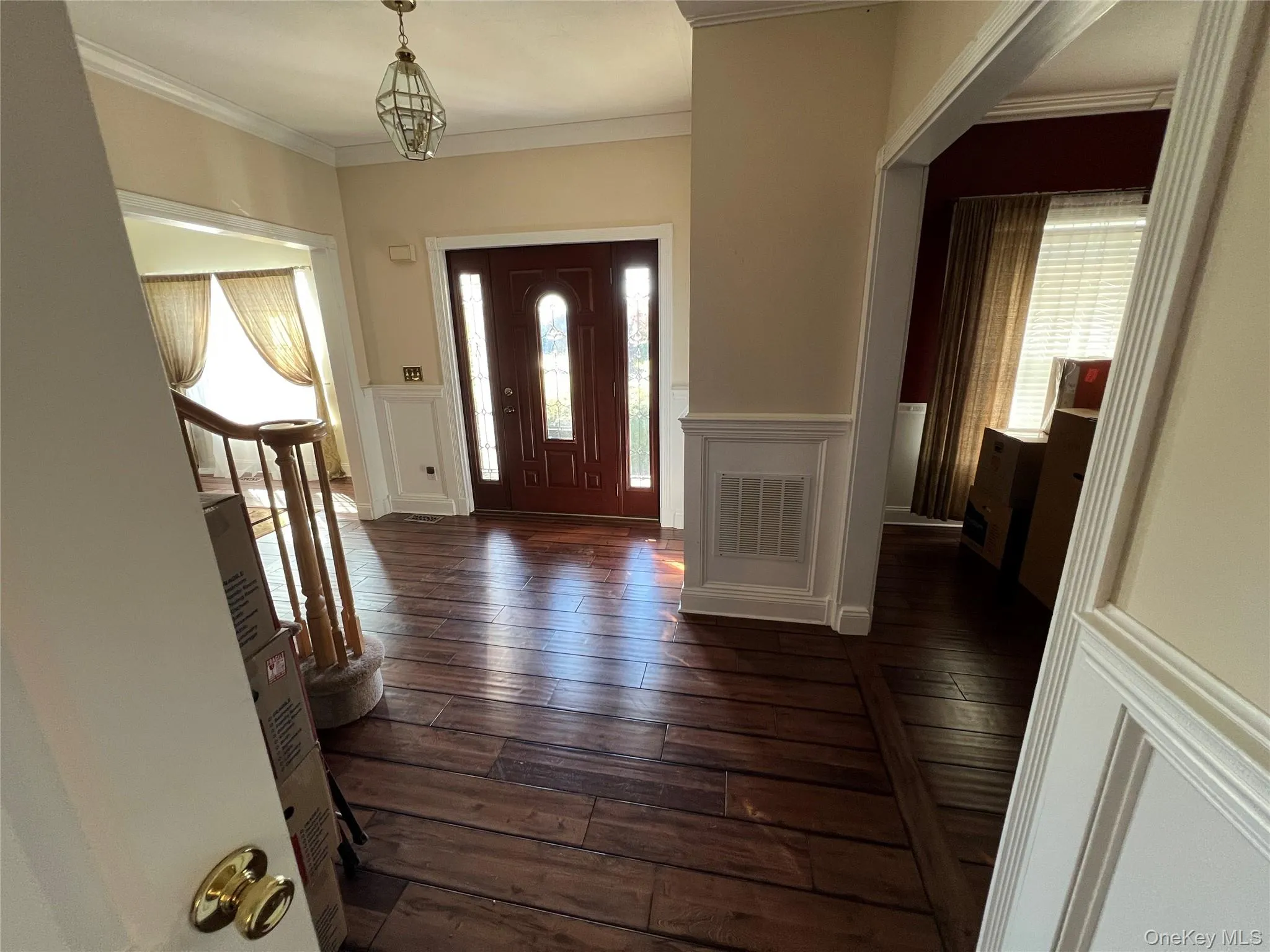 Entrance foyer with a decorative wall, a wainscoted wall, dark wood-type flooring, and ornamental molding Entrance foyer with a decorative wall, a wainscoted wall, dark wood-type flooring, and ornamental molding