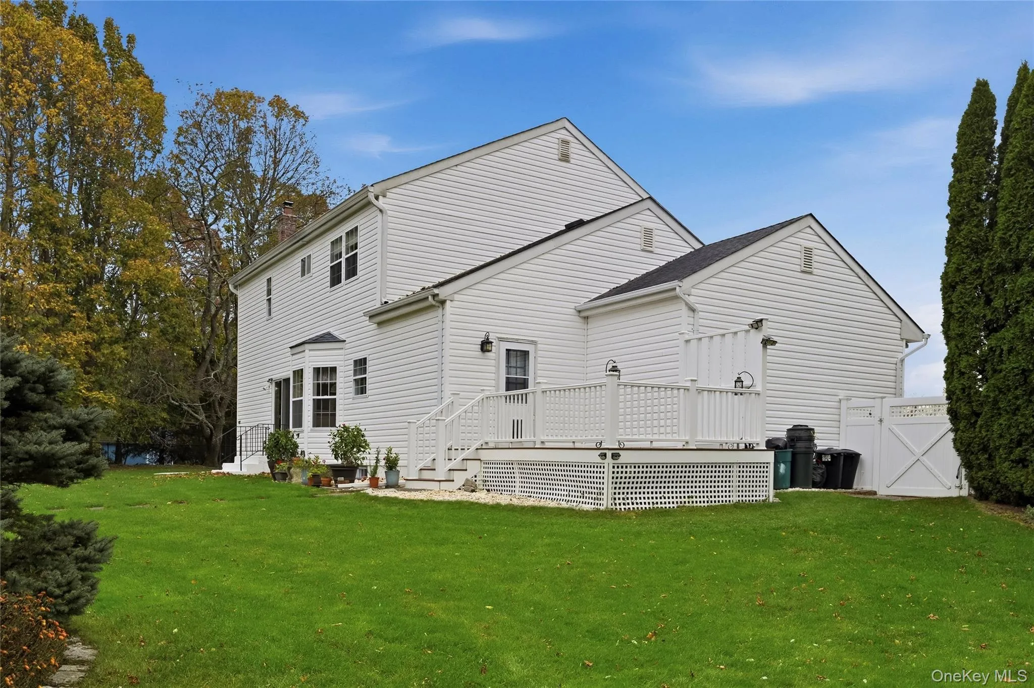 Back of house with a lawn, a deck, a chimney, and a gate Back of house with a lawn, a deck, a chimney, and a gate