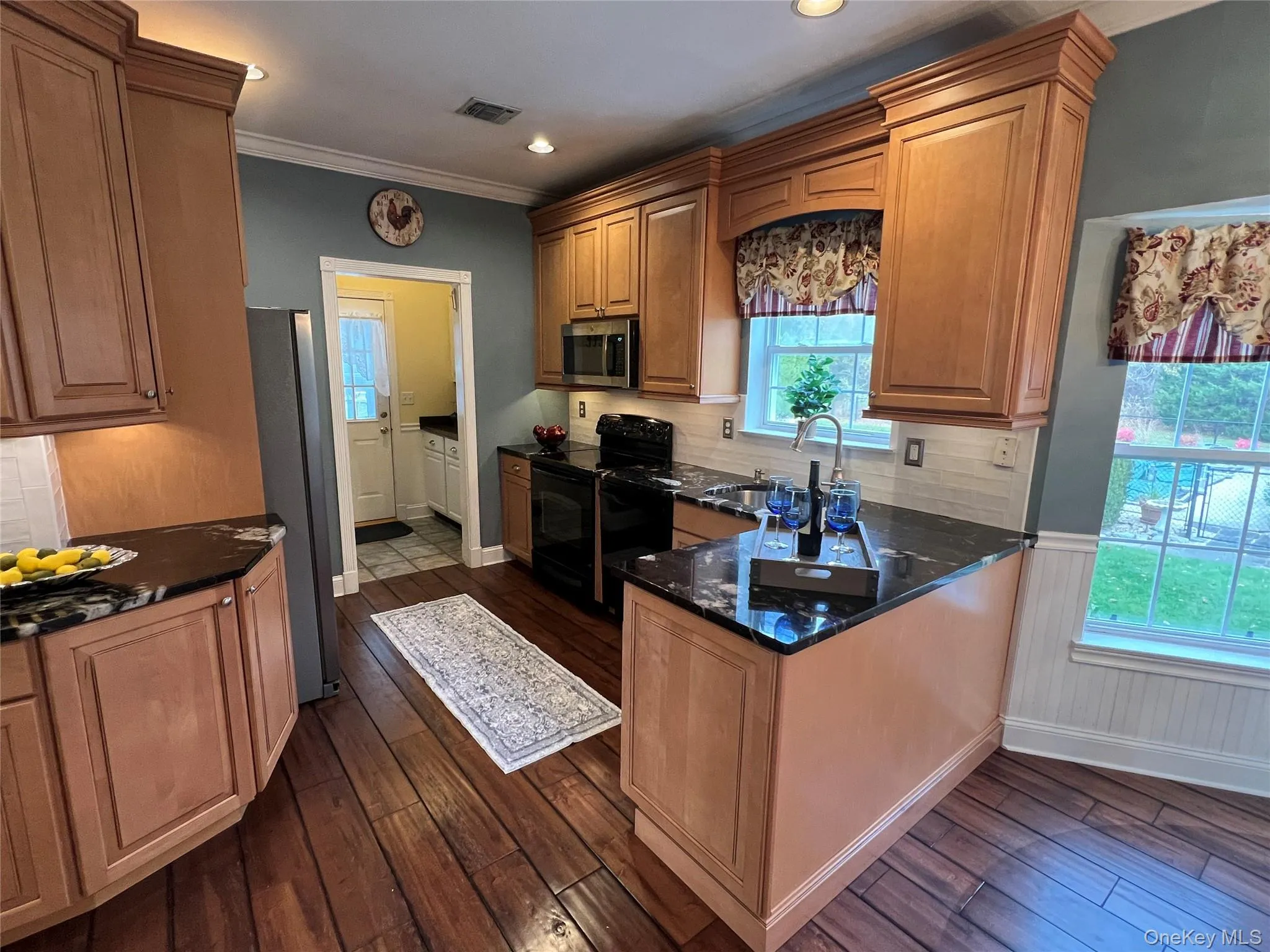 Kitchen with tasteful backsplash, ornamental molding, dark stone counters, black appliances, and dark wood finished floors Kitchen with tasteful backsplash, ornamental molding, dark stone counters, black appliances, and dark wood finished floors