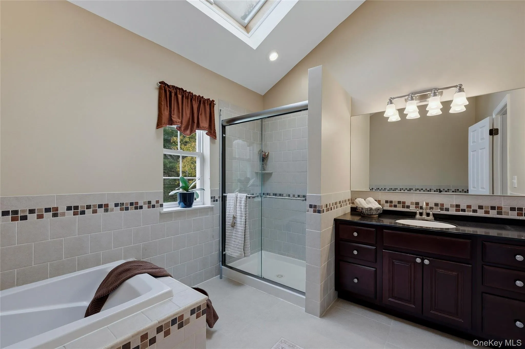 Full bathroom with a skylight, vanity, vaulted ceiling, a garden tub, and tile walls Full bathroom with a skylight, vanity, vaulted ceiling, a garden tub, and tile walls