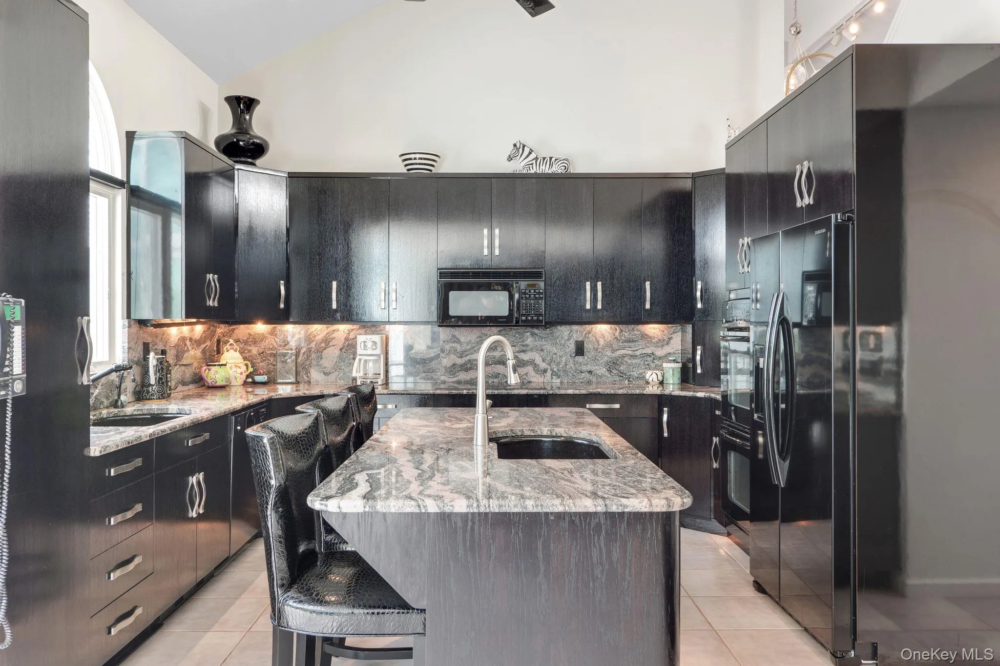 Kitchen featuring light stone counters, a breakfast bar, light tile patterned flooring, a center island with sink, and high vaulted ceiling Kitchen featuring light stone counters, a breakfast bar, light tile patterned flooring, a center island with sink, and high vaulted ceiling