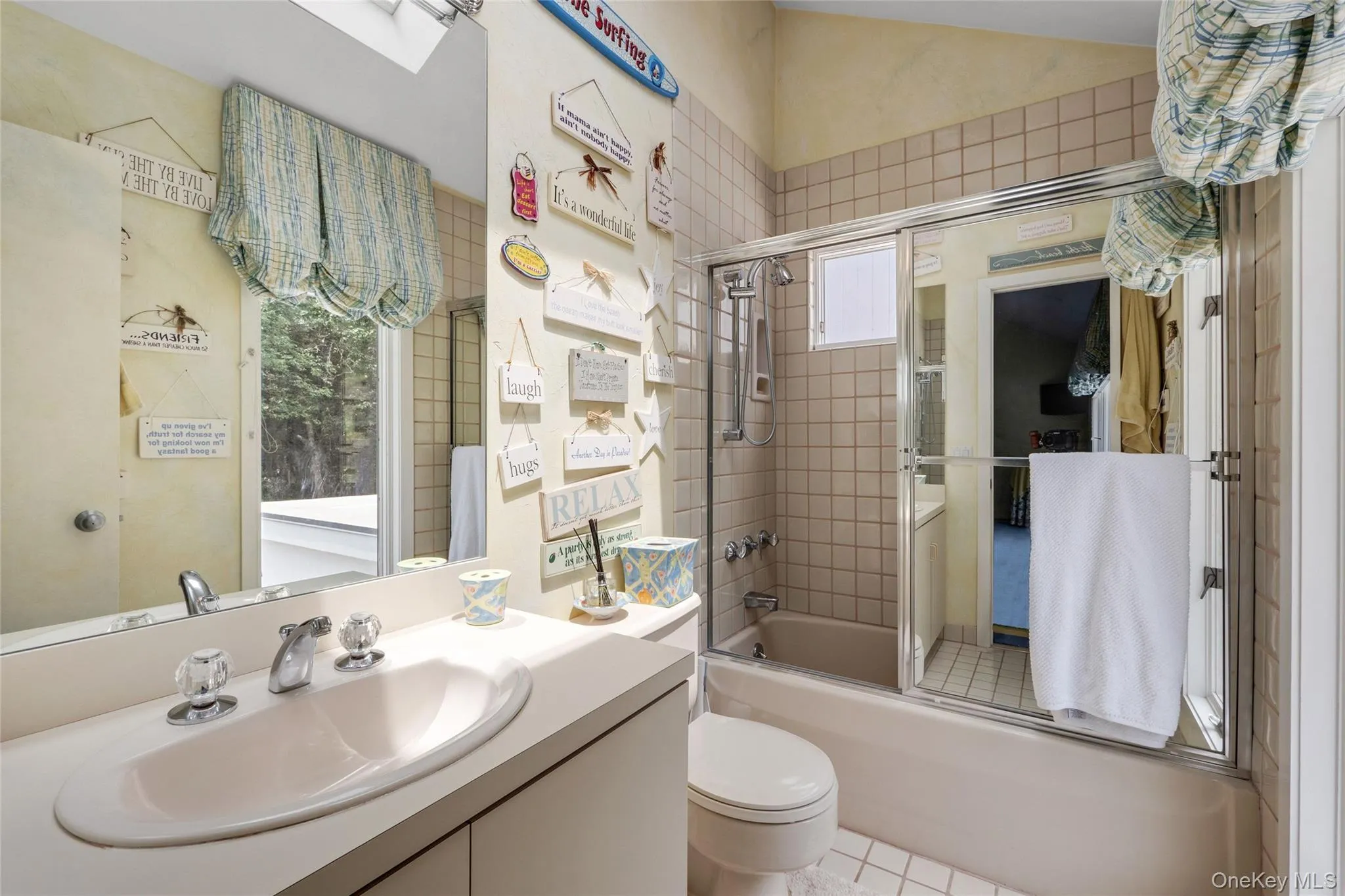 Full bathroom featuring enclosed tub / shower combo, vanity, light tile patterned flooring, and a skylight Full bathroom featuring enclosed tub / shower combo, vanity, light tile patterned flooring, and a skylight