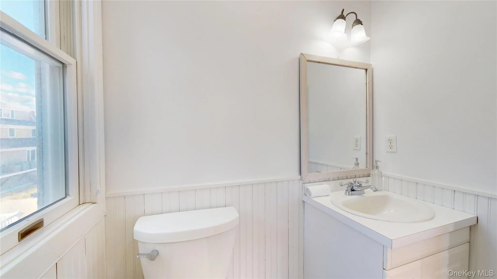 Half bath featuring healthy amount of natural light, vanity, and wainscoting Half bath featuring healthy amount of natural light, vanity, and wainscoting