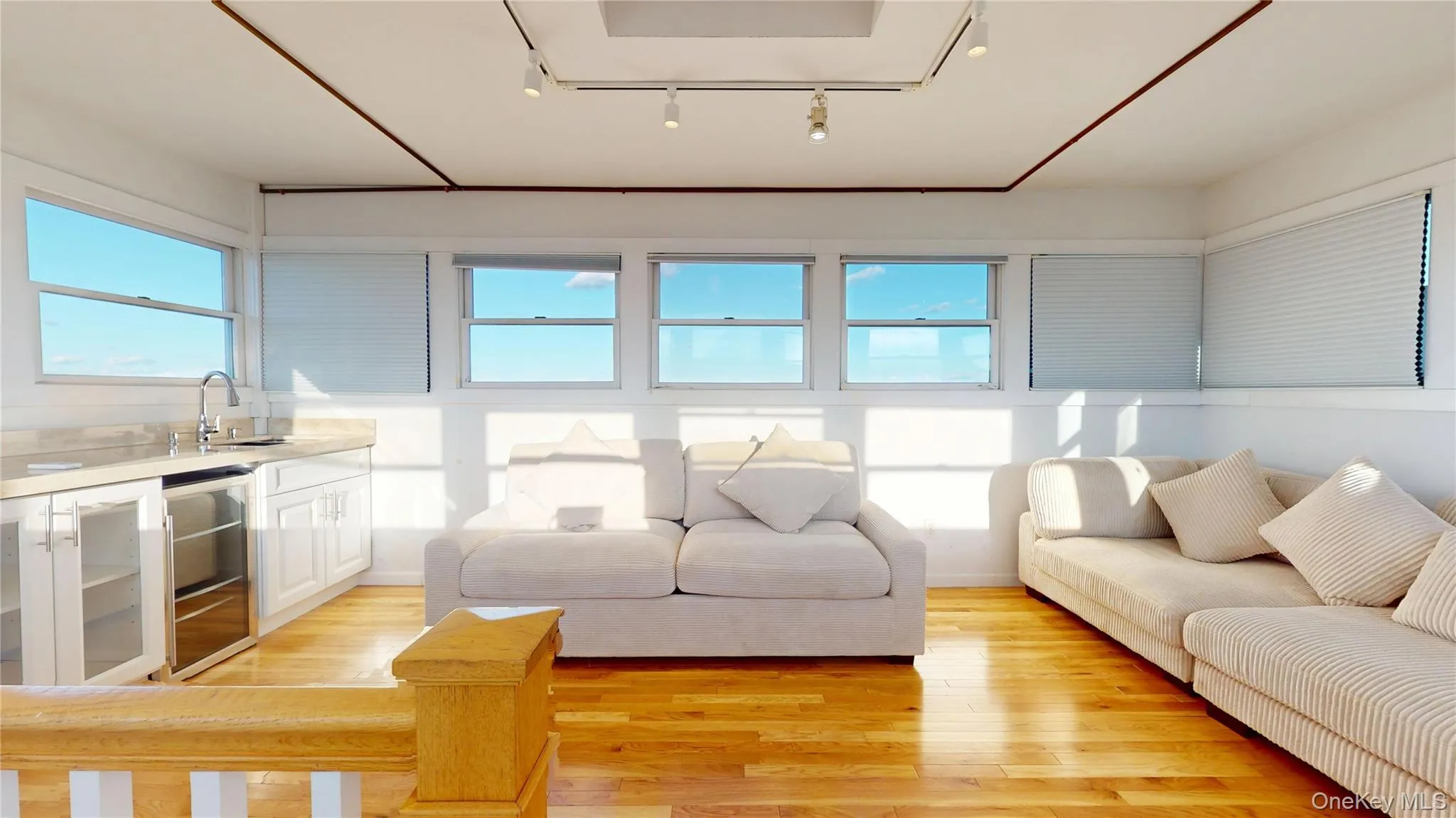 Living room featuring light wood-style flooring, track lighting, and beverage cooler Living room featuring light wood-style flooring, track lighting, and beverage cooler